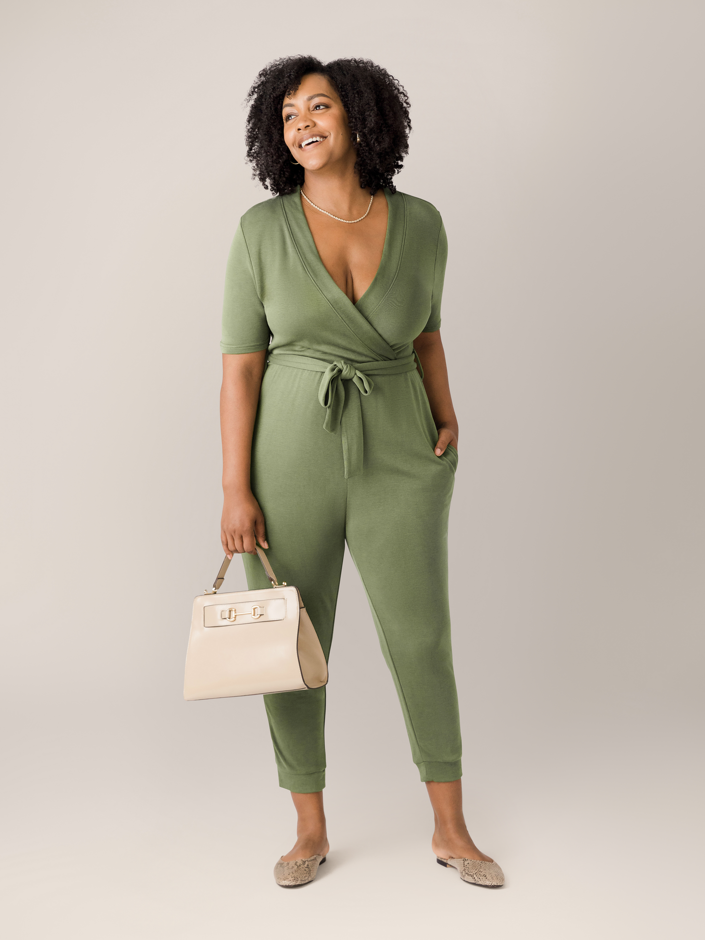 Model wearing the Around the Clock Nursing Jumpsuit in Olive with a bag.@model_info:Roxanne is 5'8" and wearing a Large.