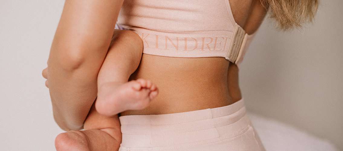 Cropped in image of model holding infant, showing Kindred Bravely bra band