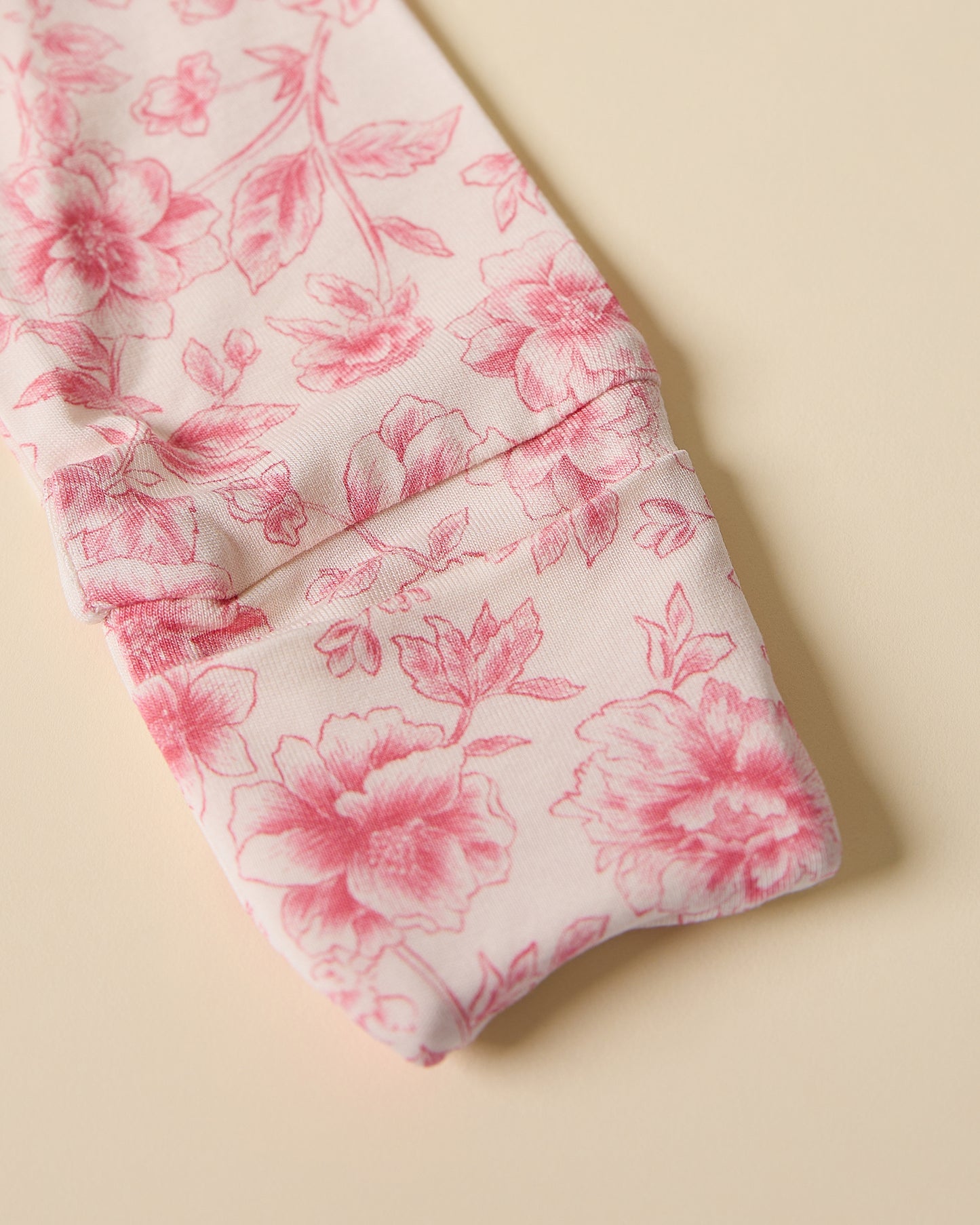 Sleeve with fold-over cuff of loral-patterned Bamboo Baby Pajama in pink toile on a beige background