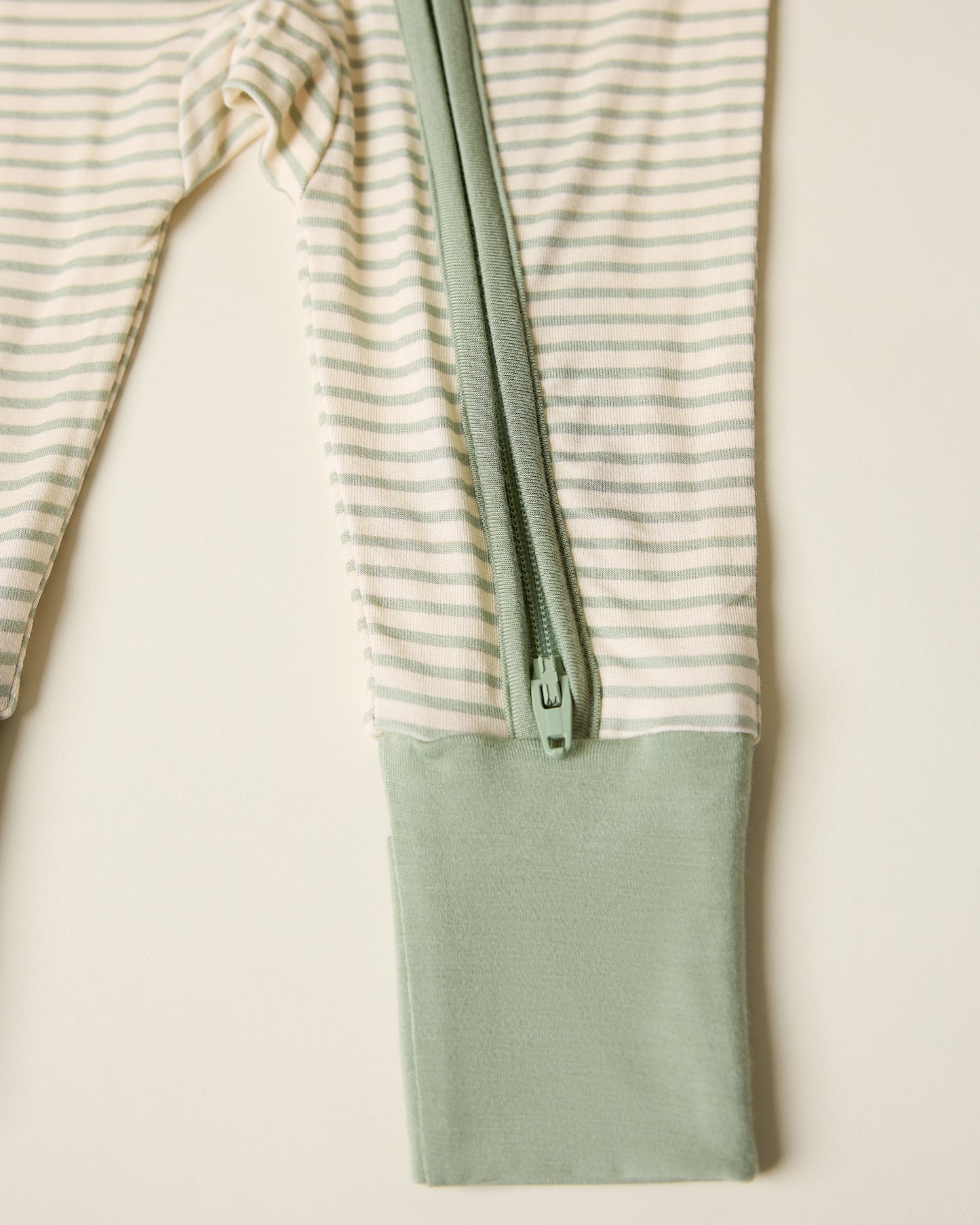 Bamboo Baby Pajama with sage candy stripe pattern, showing zipper, on a beige background