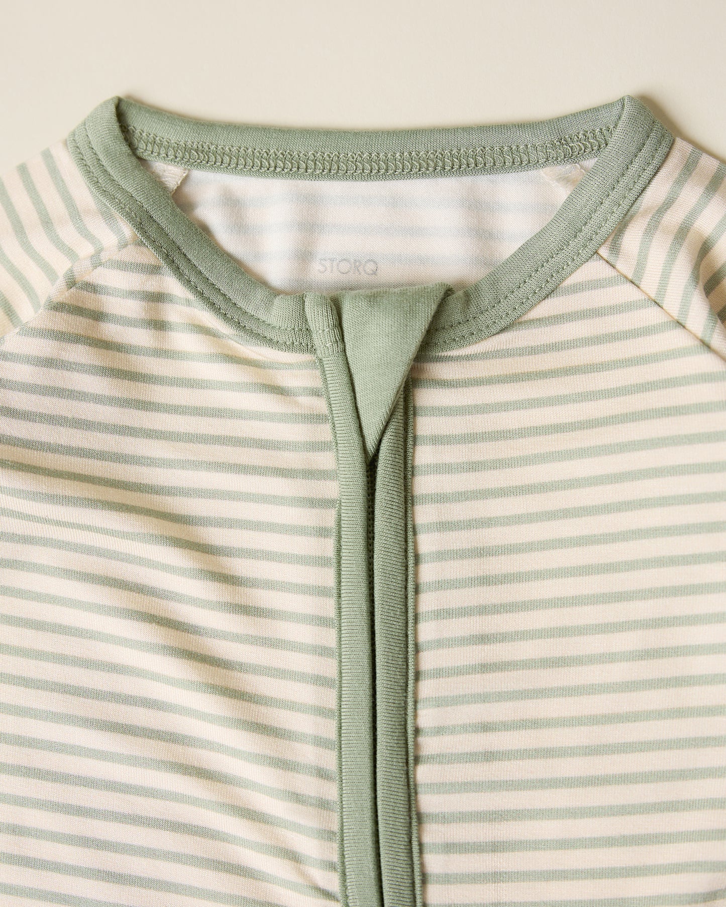 Close-up of the Bamboo Baby Pajama with sage candy stripe pattern on a beige background