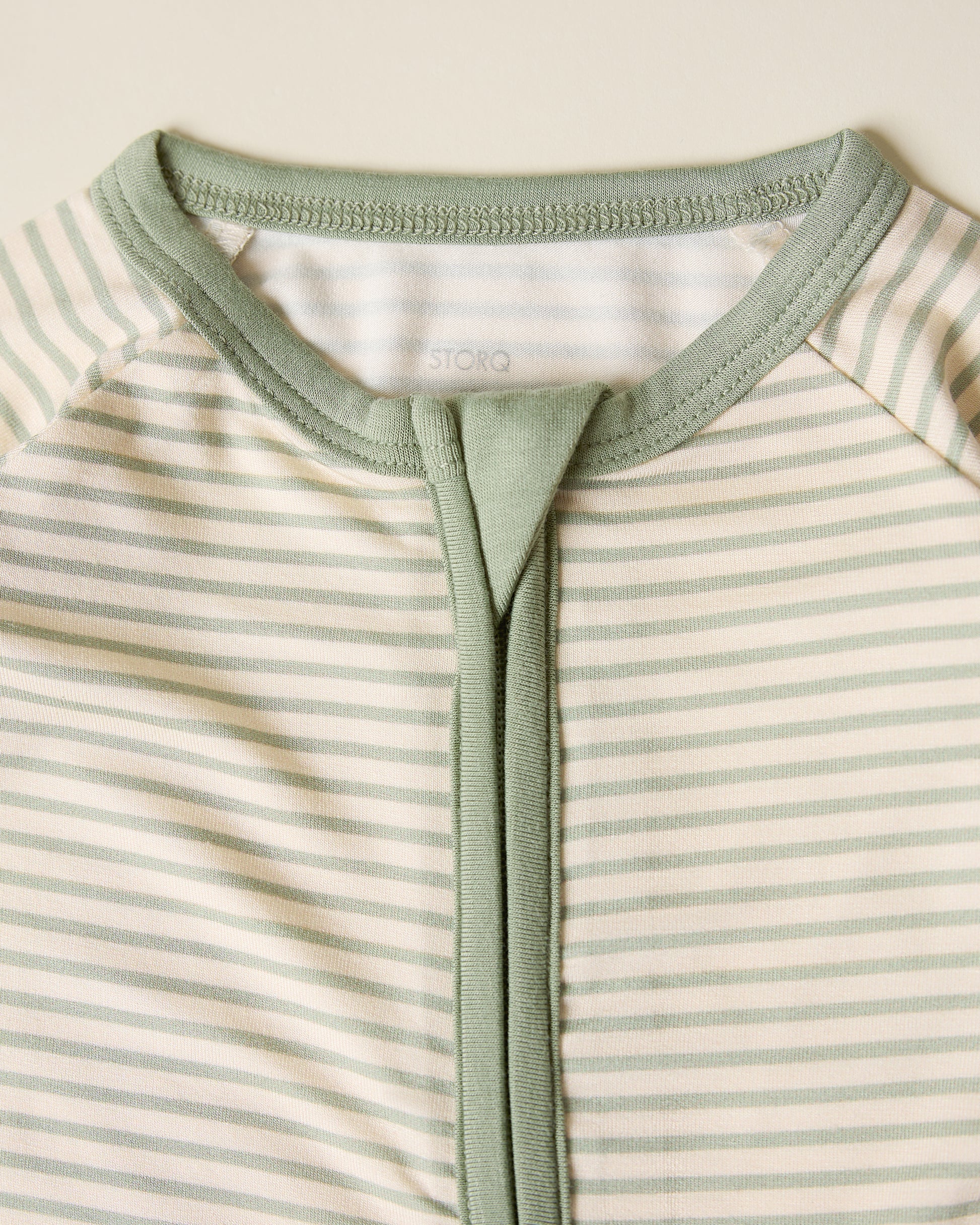 Close-up of the Bamboo Baby Pajama with sage candy stripe pattern on a beige background