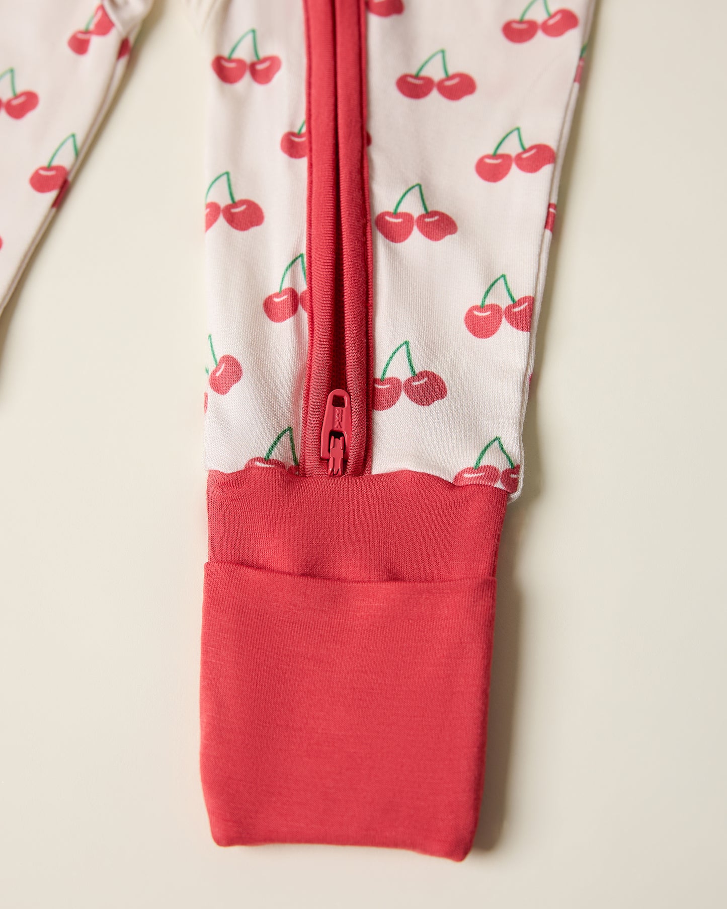 Close-up of a children's outfit with cherry pattern and red zipper on a light background