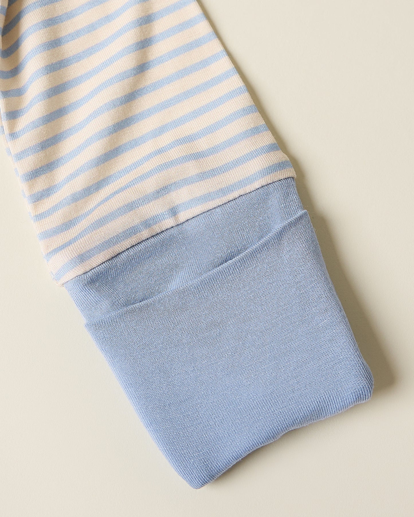 Bamboo Baby Pajama with blue candy stripe pattern showing foldover cuff on a beige background