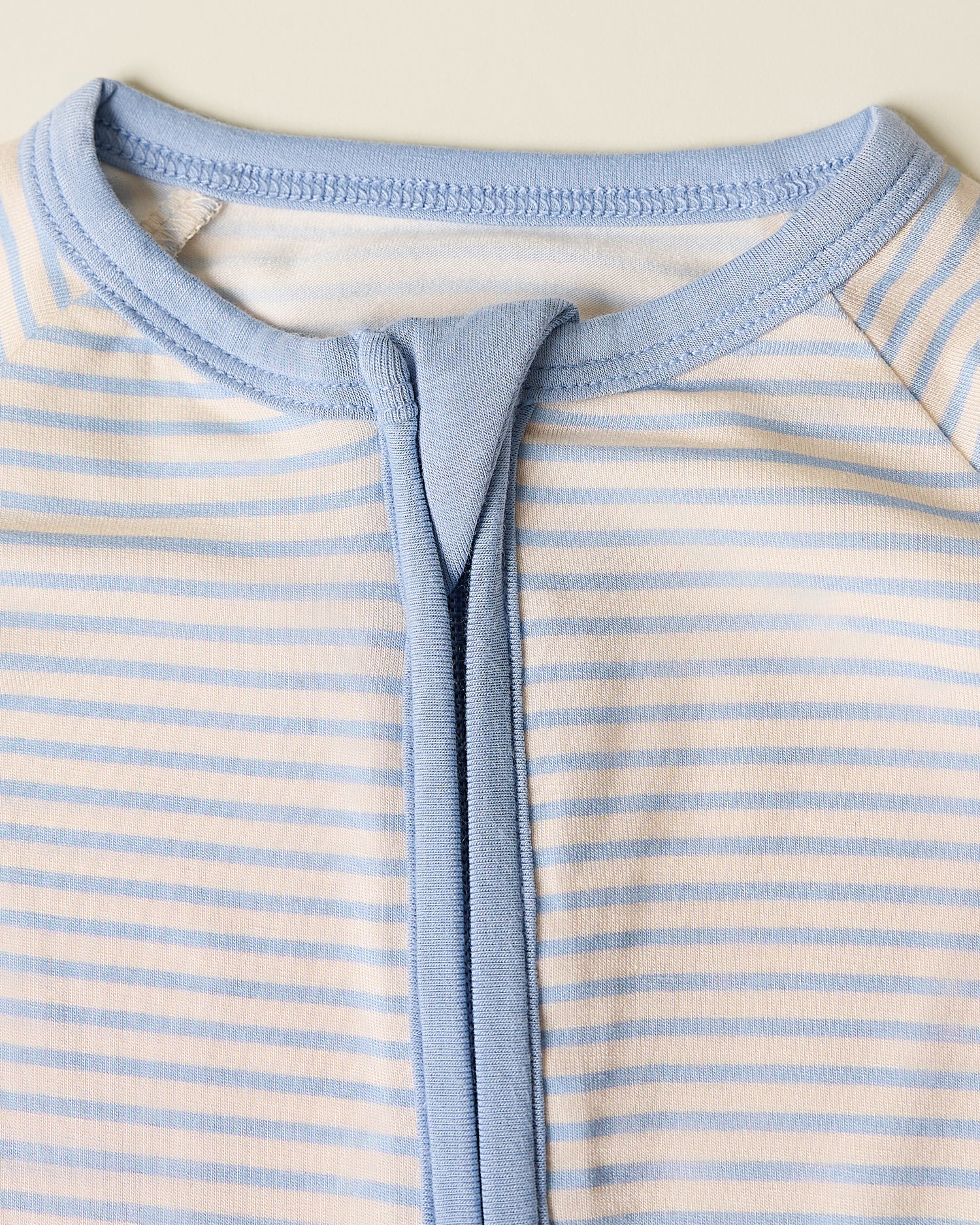 Close up of Bamboo Baby Pajama with blue candy stripe pattern on a beige background