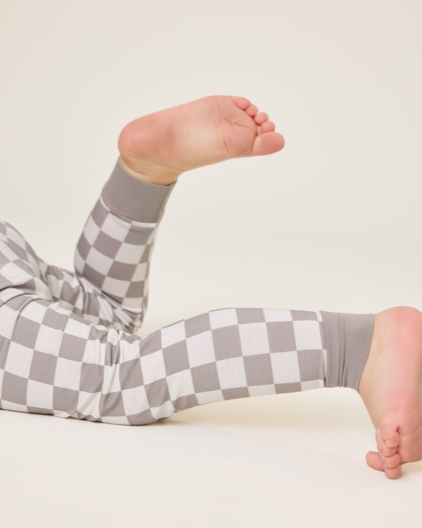 Close up of Baby lying down wearing the Bamboo Baby Two-Piece Pajama Set in Taupe Checker print