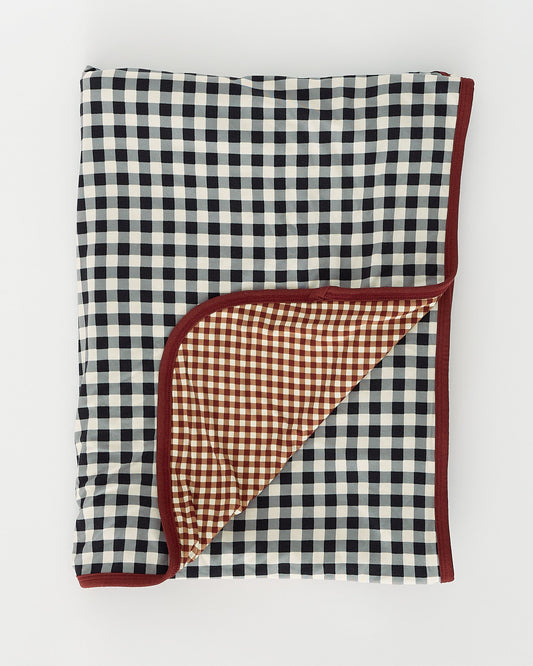 Bamboo Blanket in Black Gingham pulled back to reveal reversible design, on an off white background.