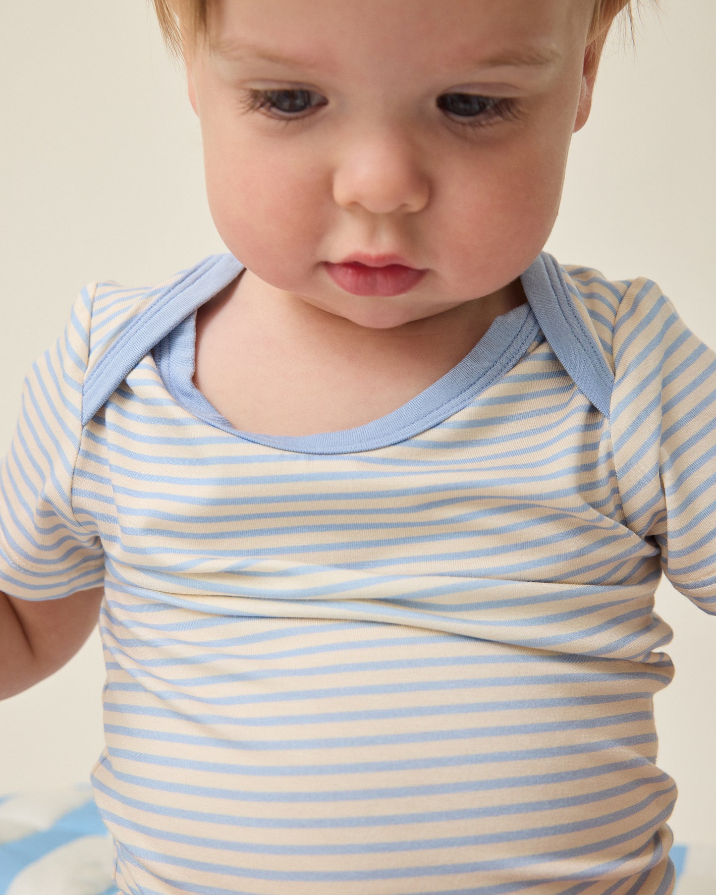 Baby wearing a blue and white striped onesie against a neutral background