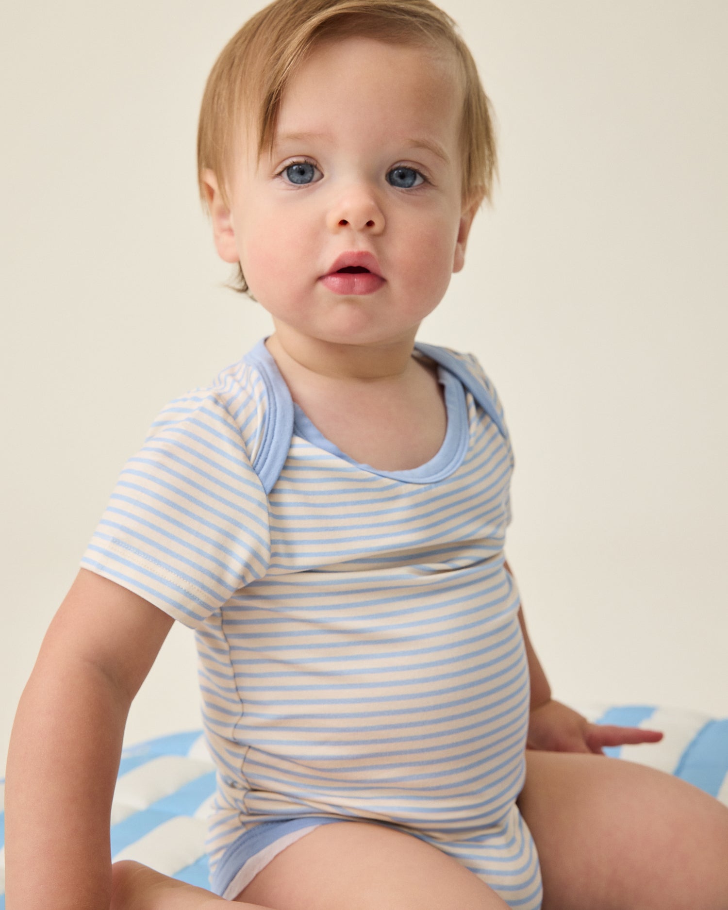 Baby wearing a blue and white striped onesie against a neutral background@model_info:Noa is wearing 6-12 months.