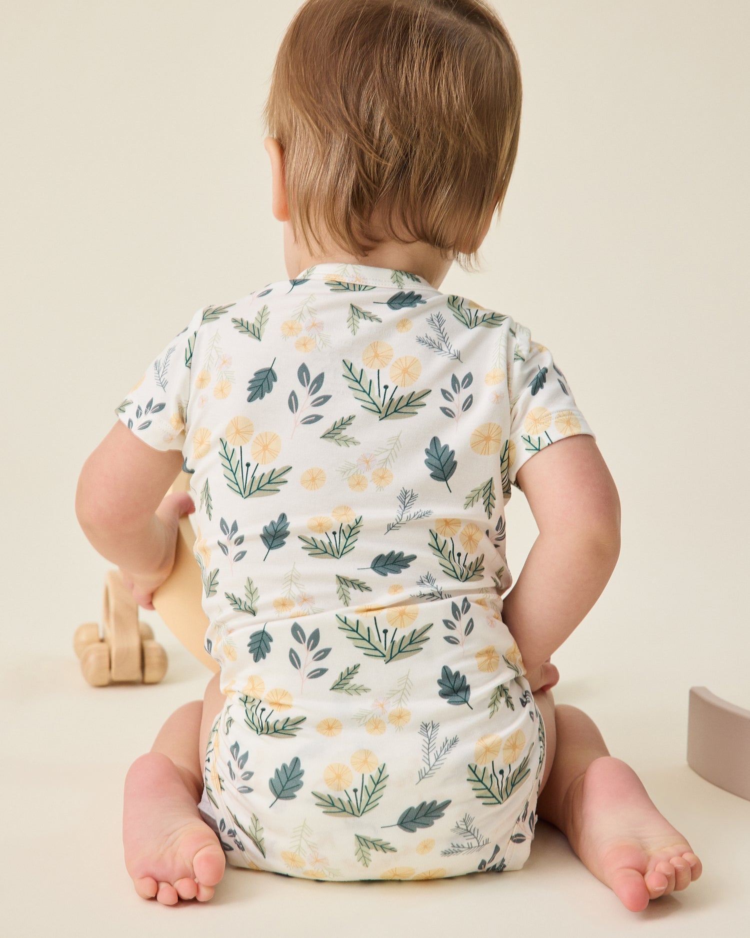 Baby wearing a floral onesie sitting on a beige surface