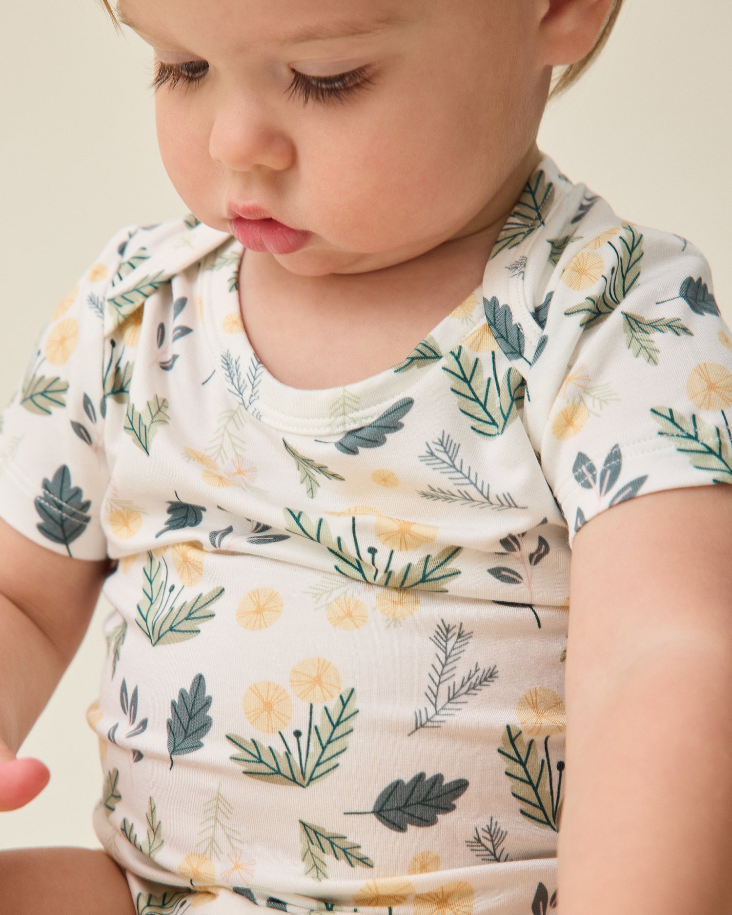 Baby wearing a floral onesie on a beige background@model_info:Noa is wearing 6-12 months.