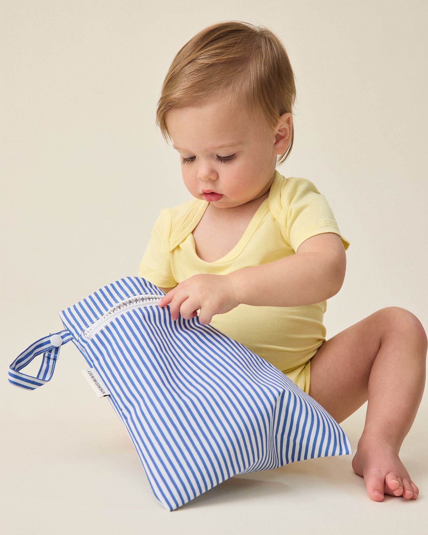 Baby holding thin blue stripe bag of Wet/Dry Bag Set in Stripe print on a beige background