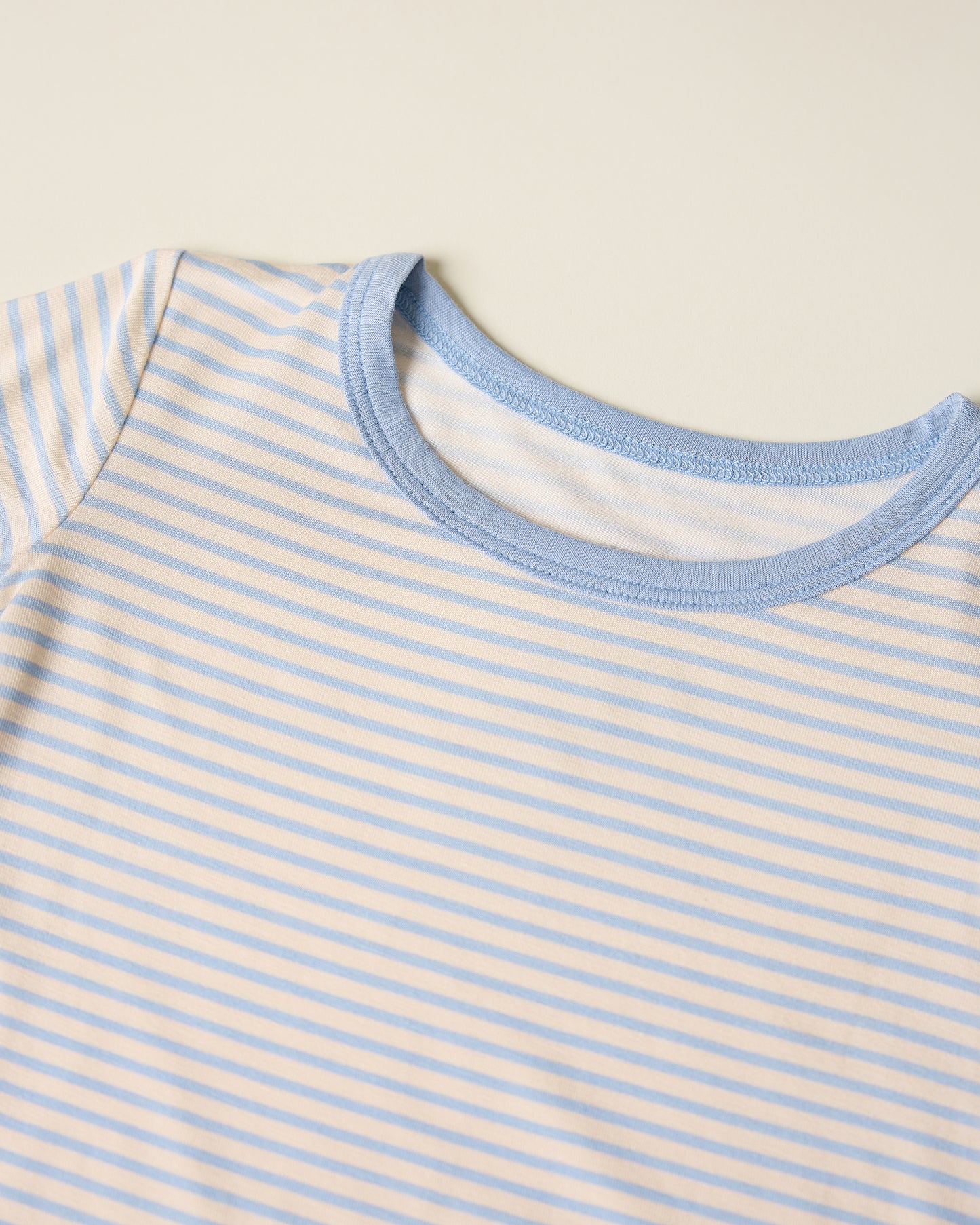 Close-up of children's striped short sleeve and shorts pajama set with blue stripes and accents on a beige background