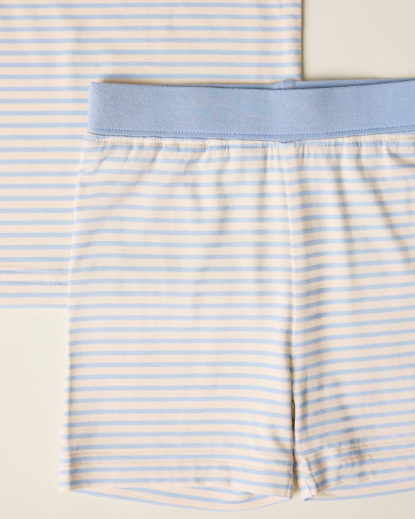 Close-up of children's striped short sleeve and shorts pajama set with blue stripes and accents on a beige background