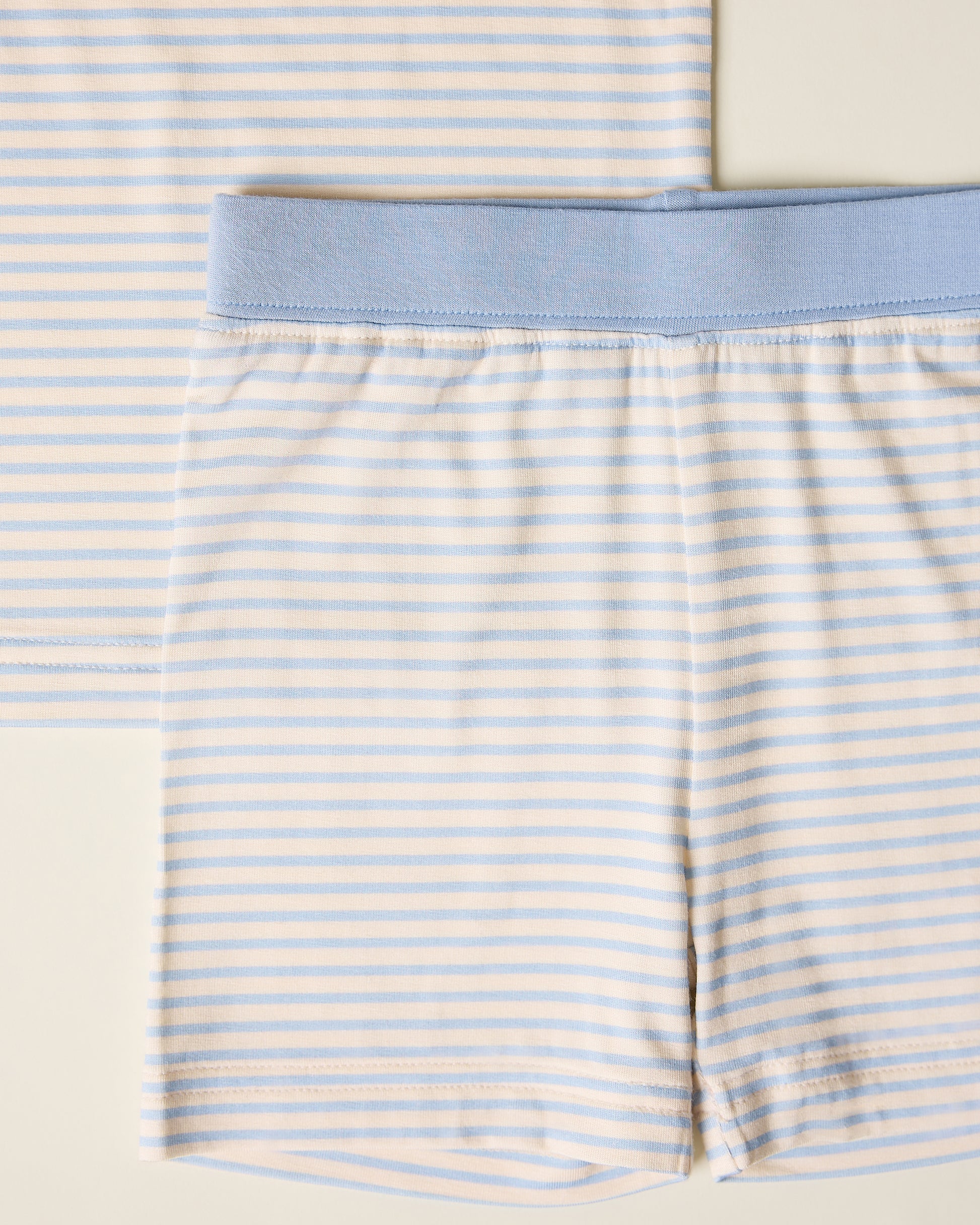 Close-up of children's striped short sleeve and shorts pajama set with blue stripes and accents on a beige background