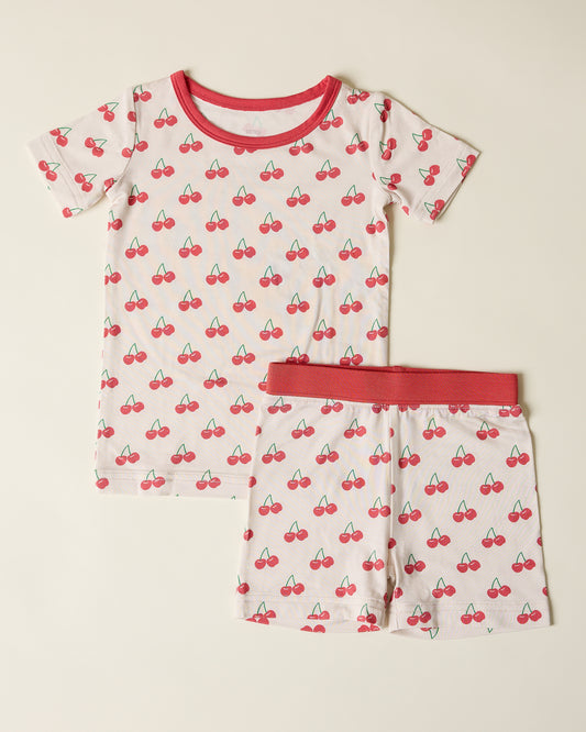Children's short sleeve and shorts pajama set with cherry pattern on a beige background
