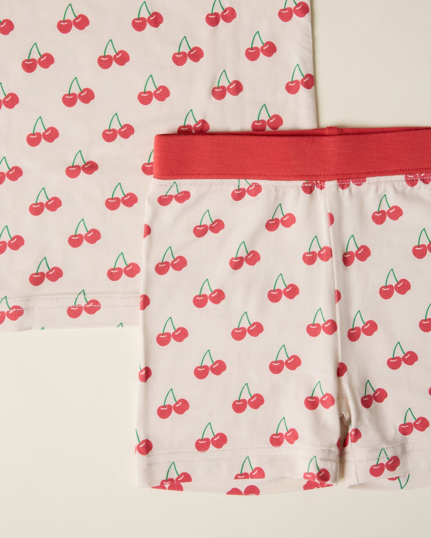 Close-up of children's short sleeve and shorts pajama set with cherry pattern on a beige background