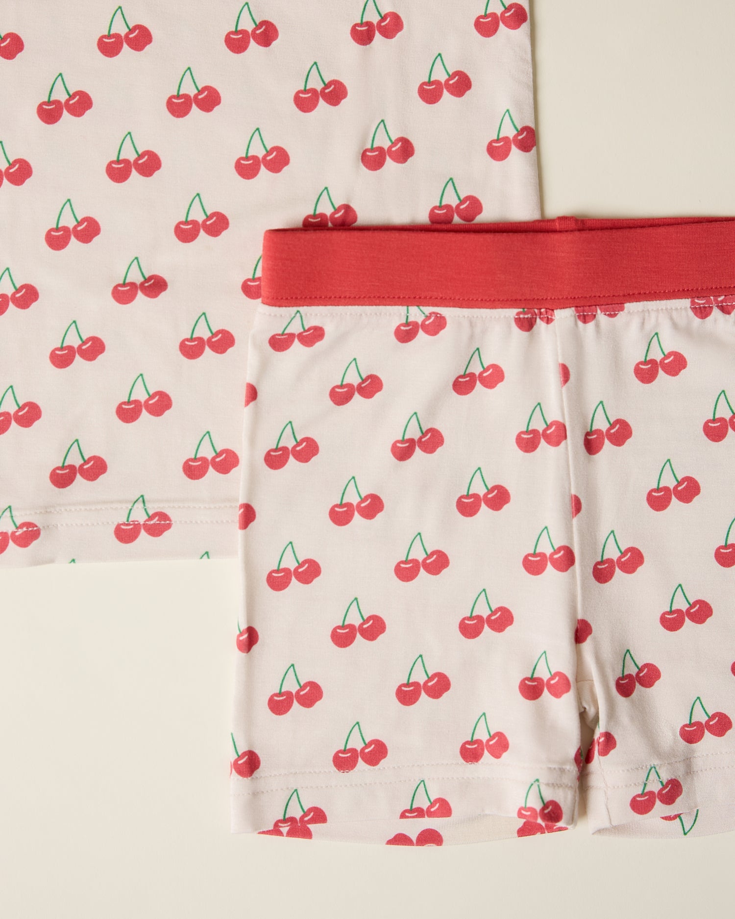 Close-up of children's short sleeve and shorts pajama set with cherry pattern on a beige background