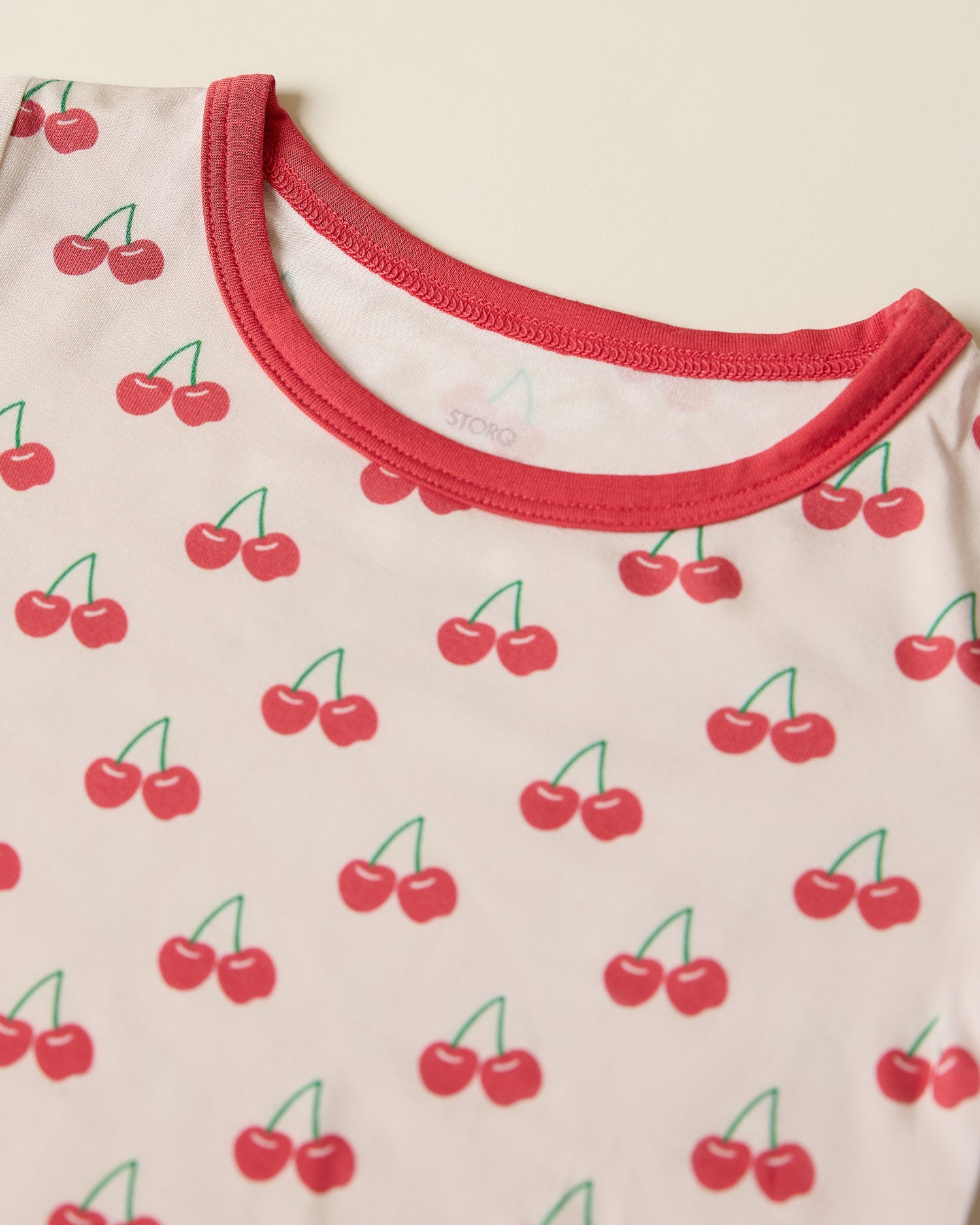 Close-up of children's short sleeve and shorts pajama set with cherry pattern on a beige background