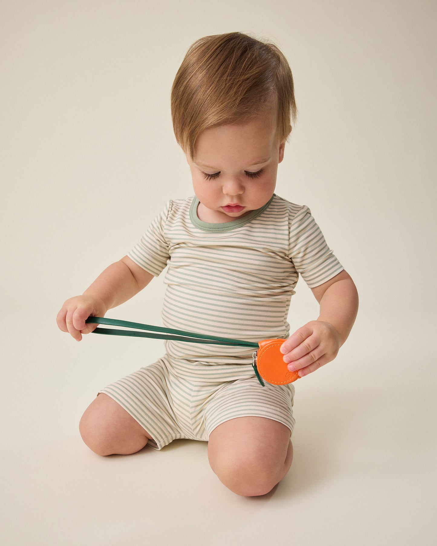Child playing with a toy and wearing the Bamboo Short Sleeve & Shorts Set in sage green stripe on a plain background