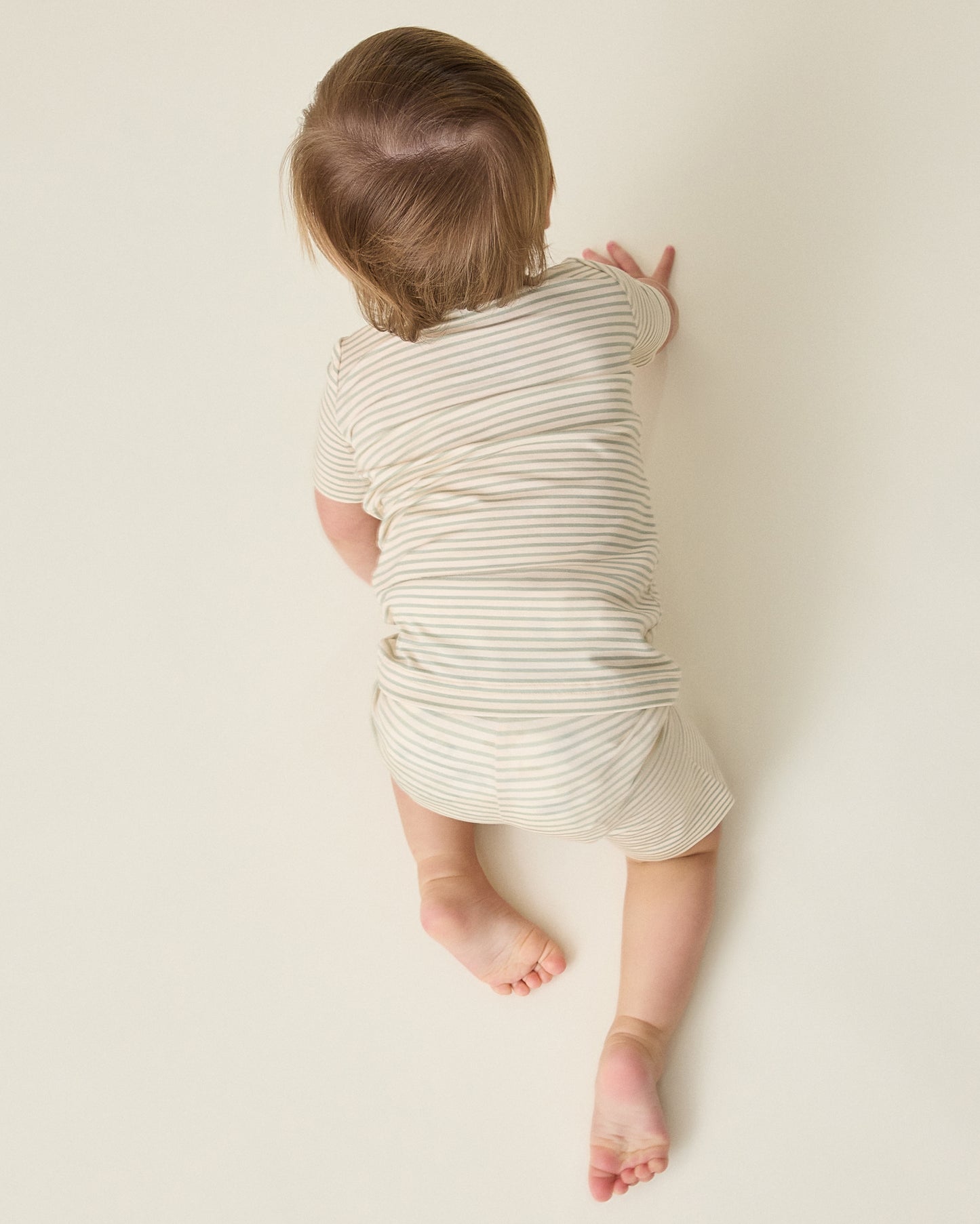 Child in the Bamboo Short Sleeve & Shorts Set in sage green stripe crawling against a plain background