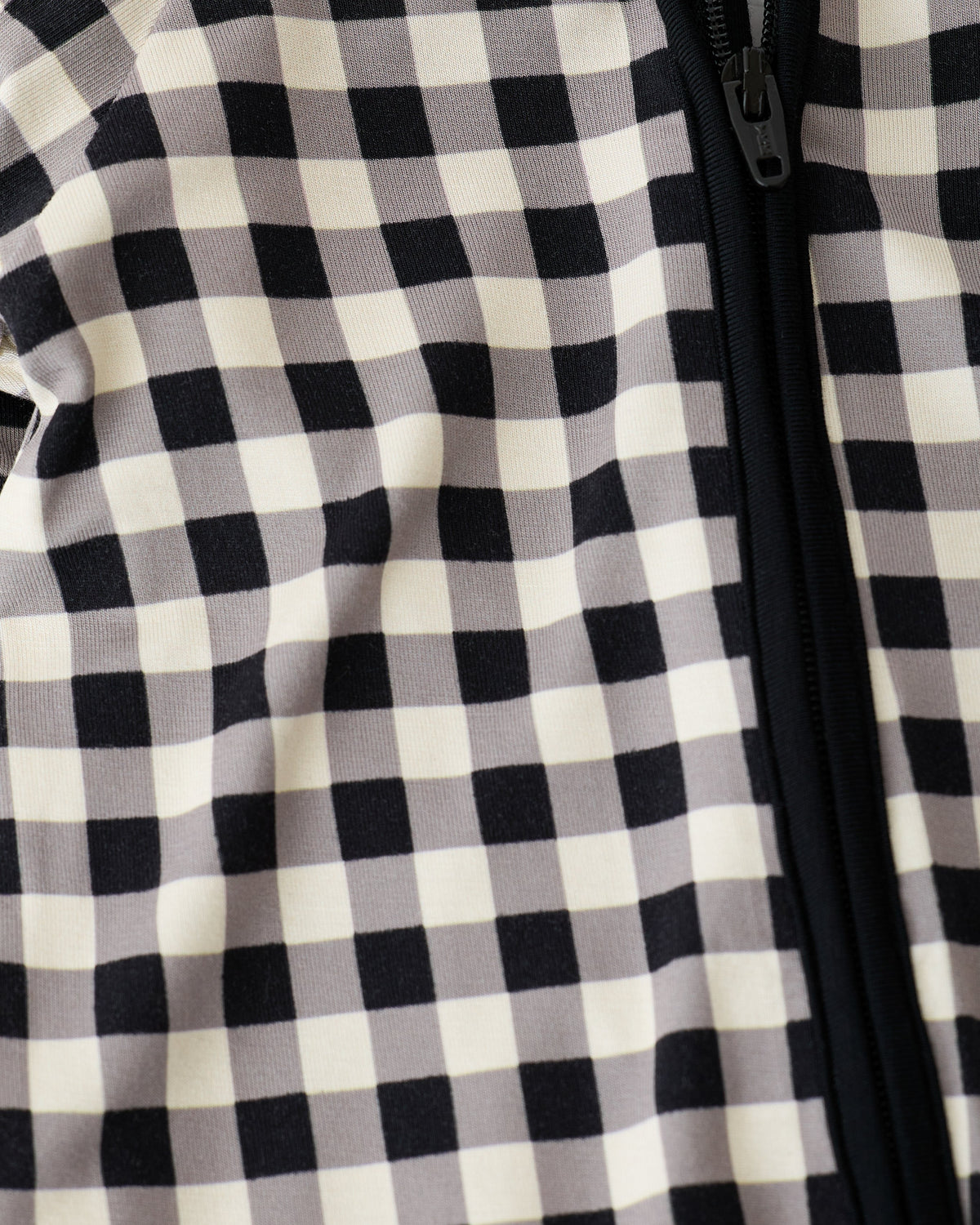 Close up of zipper detail on Bamboo Baby Pajama in Black Gingham on an off white background.