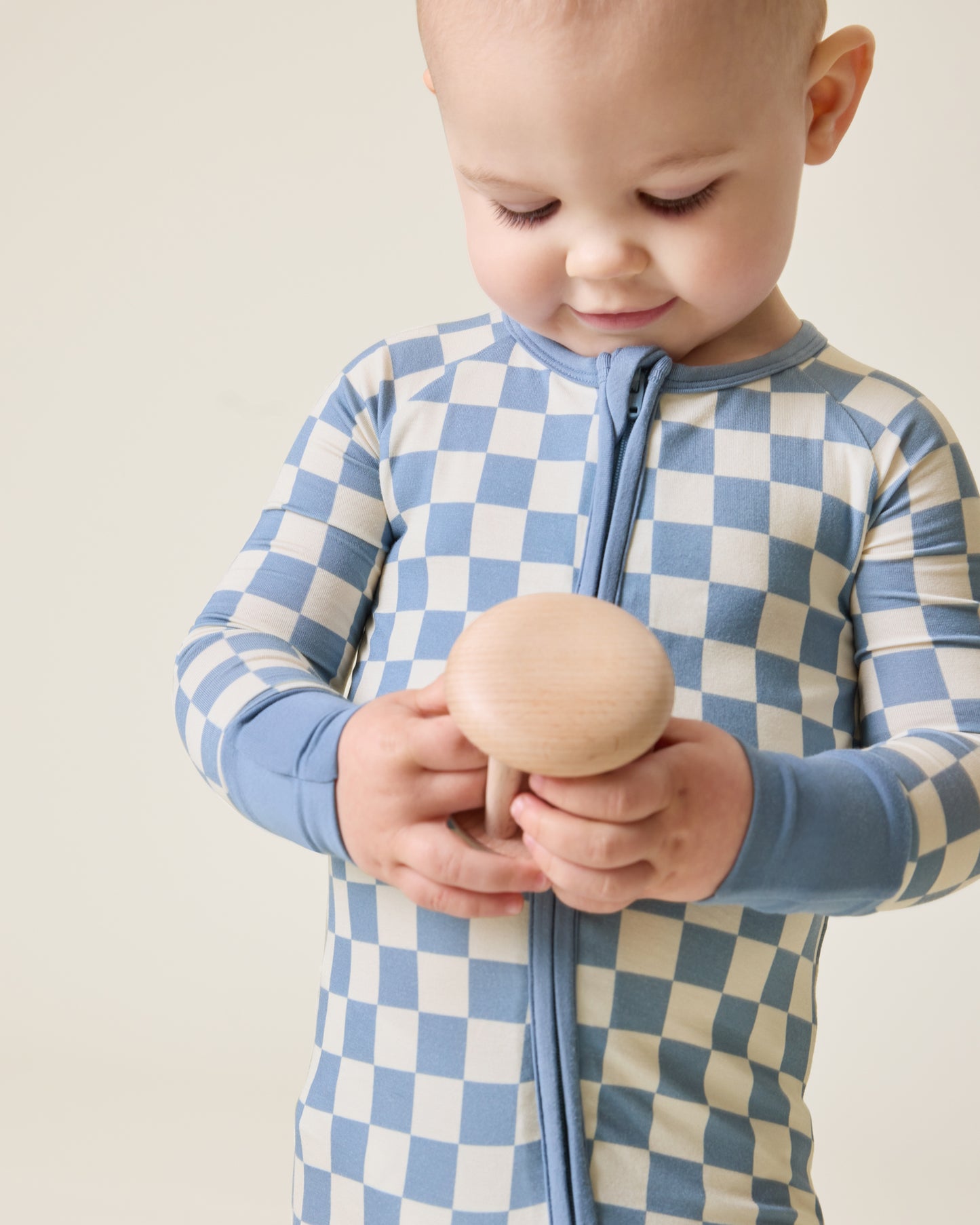 Baby holding a wooden toy wearing the Bamboo Baby Pajama in Blue Checker print