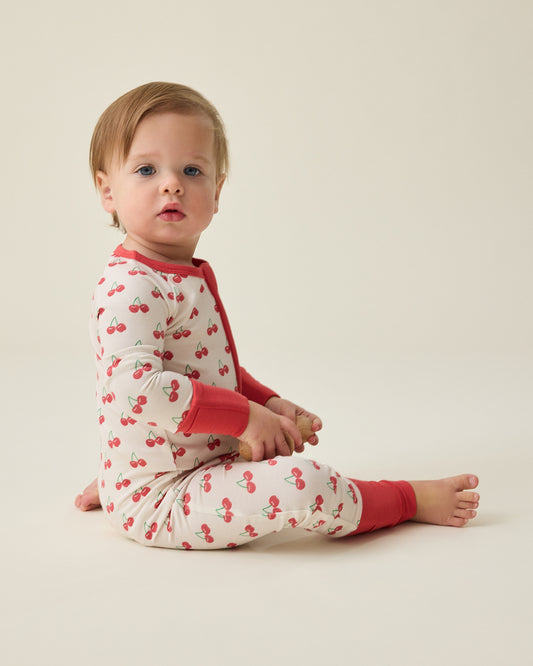 Baby wearing the Bamboo Baby Pajama with cherry pattern sitting on a beige background@model_info:Noa is wearing 6-12 months.