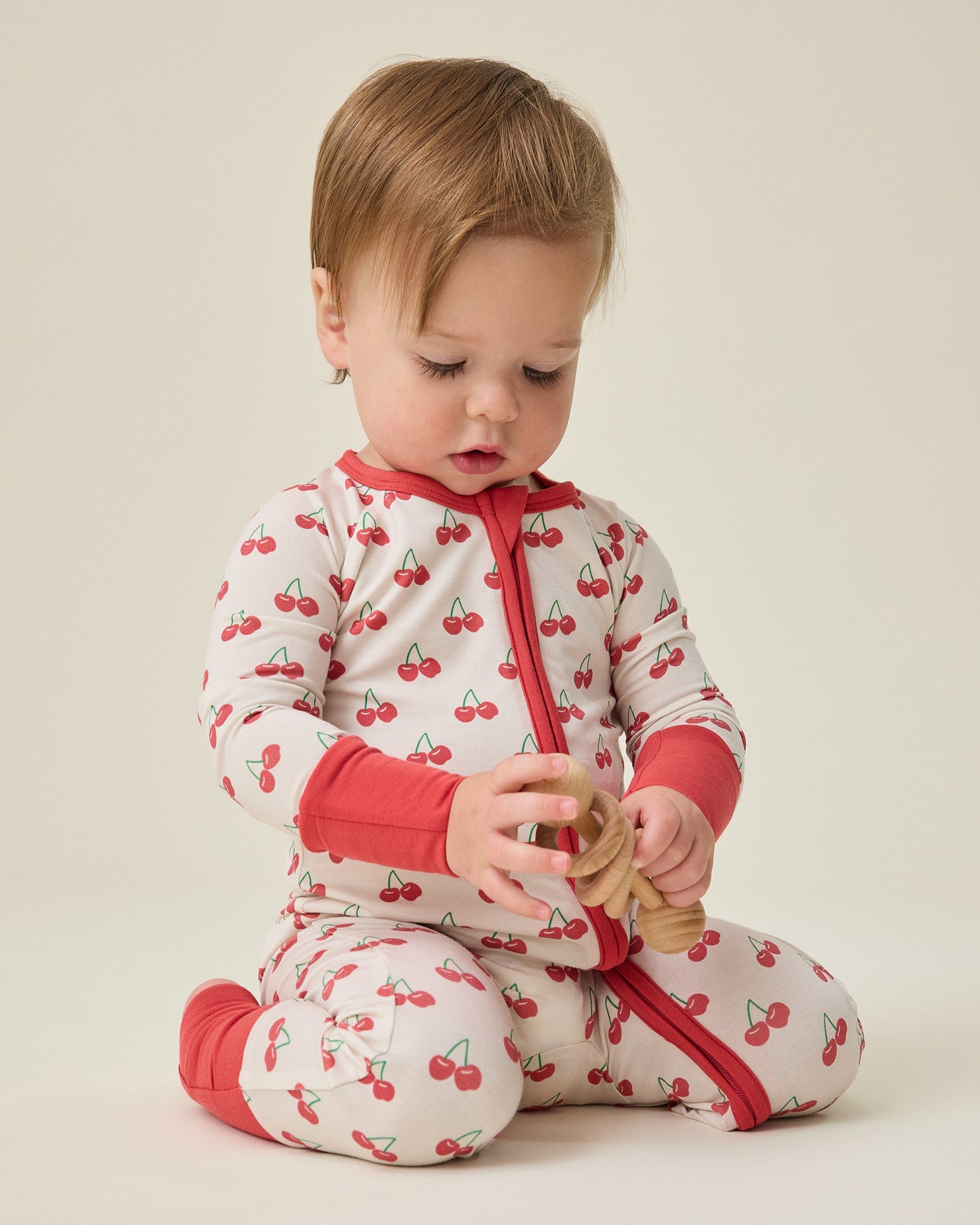 Baby wearing the Bamboo Baby Pajama with cherry pattern sitting on a beige background