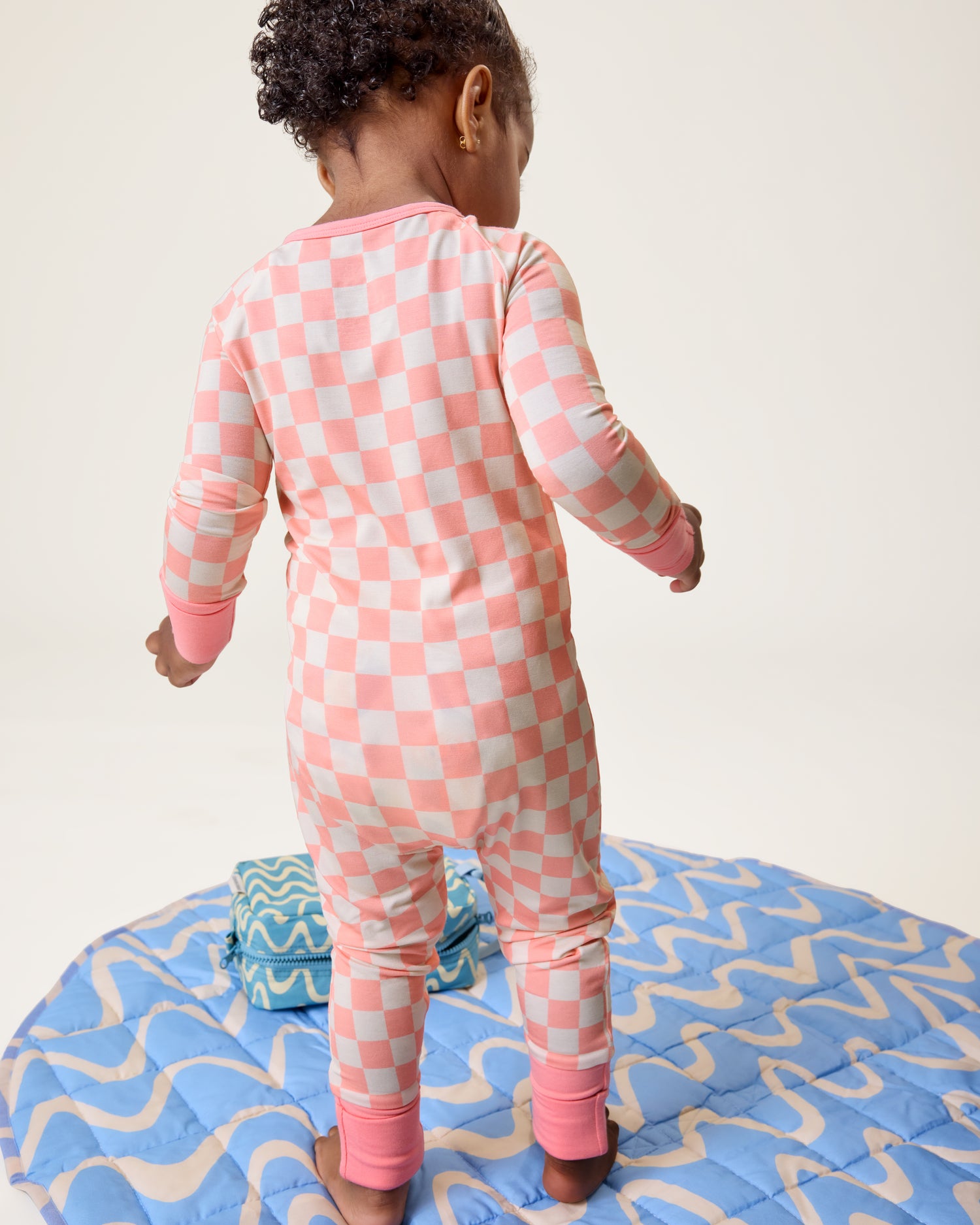 Child wearing a pink checkered onesie standing on the The Inside/Outside Play Mat in Blue Waves print