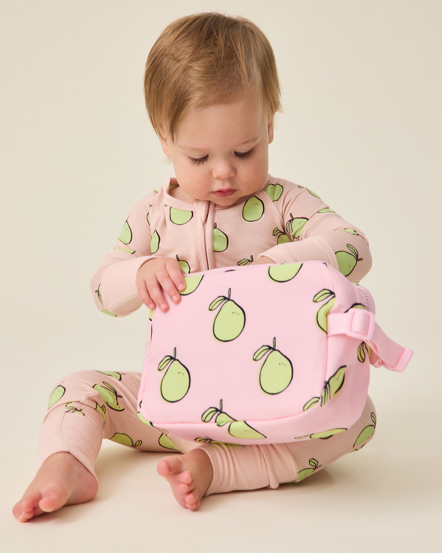 Child holding a pink Mini Cooler Bag with green pomelo patterns on a beige background