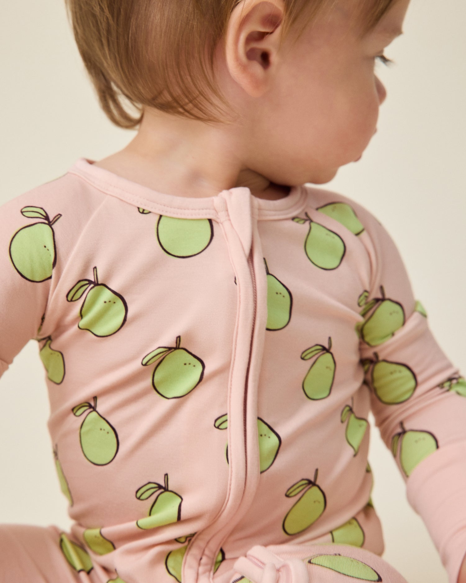 Baby wearing a pink outfit with green pomelo patterns on a light background