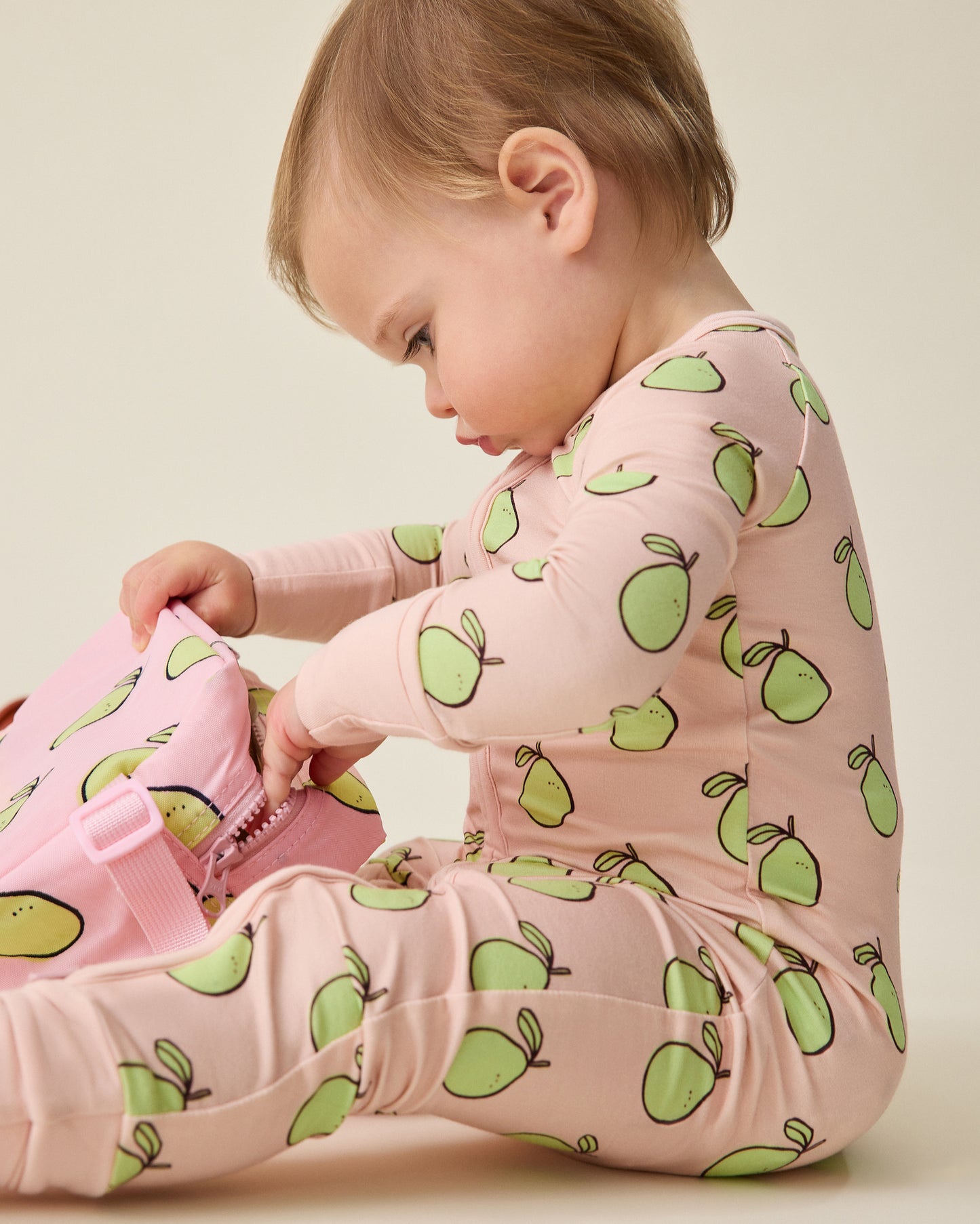 Baby wearing a pink onesie with green pomelo patterns on a beige background