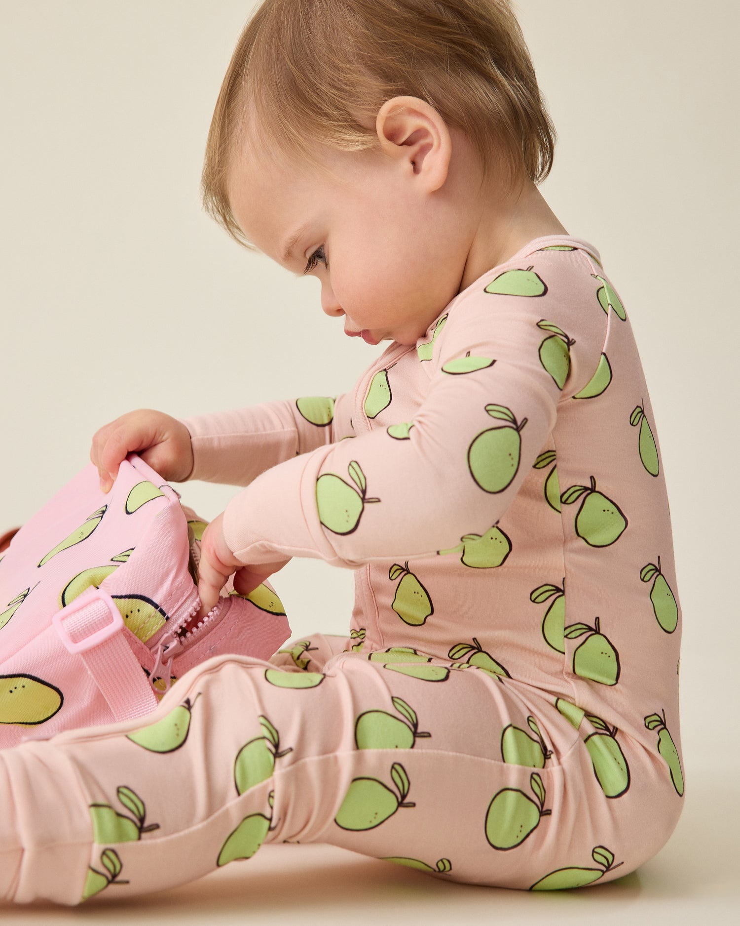 Baby wearing a pink onesie with green pomelo patterns on a beige background