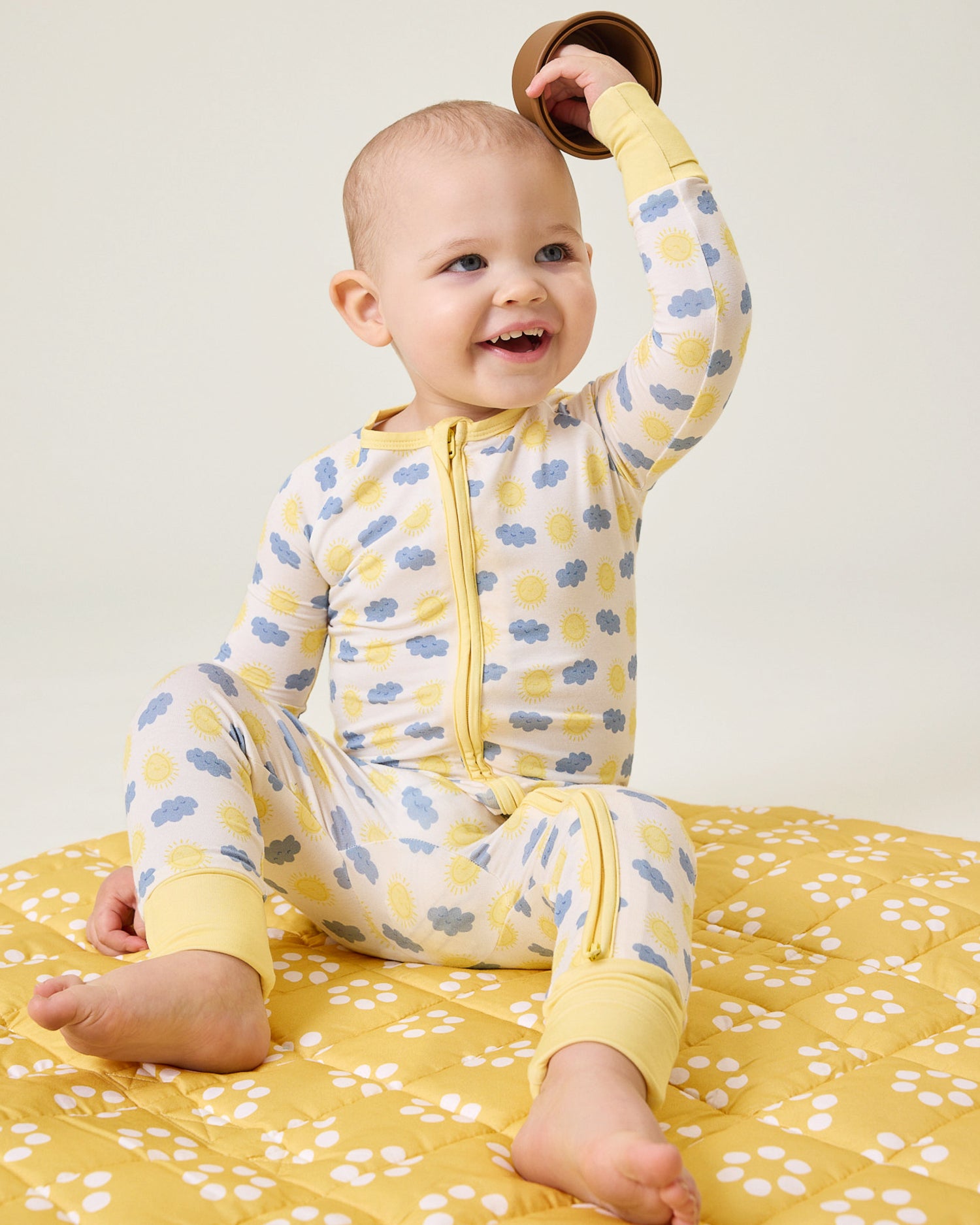 Baby in Sunny Day patterned pajama sitting on the Inside/Outside Play Mat in Sunshine Dots print