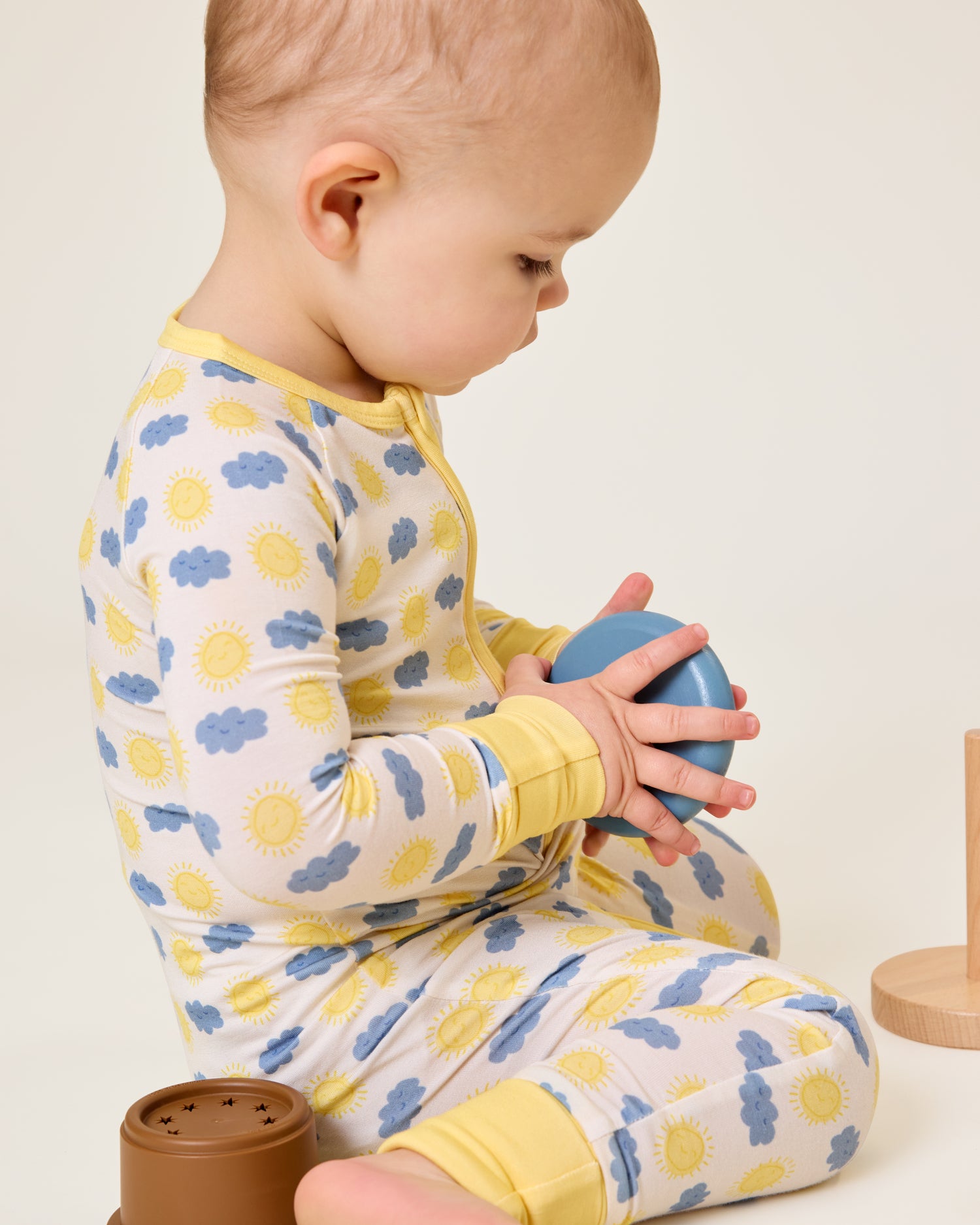 Baby playing with a wooden toy wearing the Bamboo Baby Pajama in Sunny Day print
