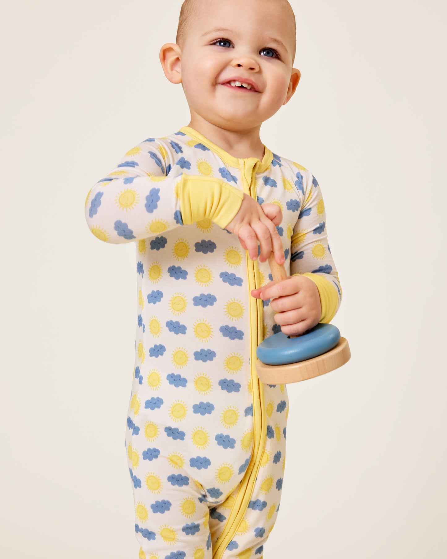 Baby holding a wooden toy wearing the Bamboo Baby Pajama in Sunny Day print