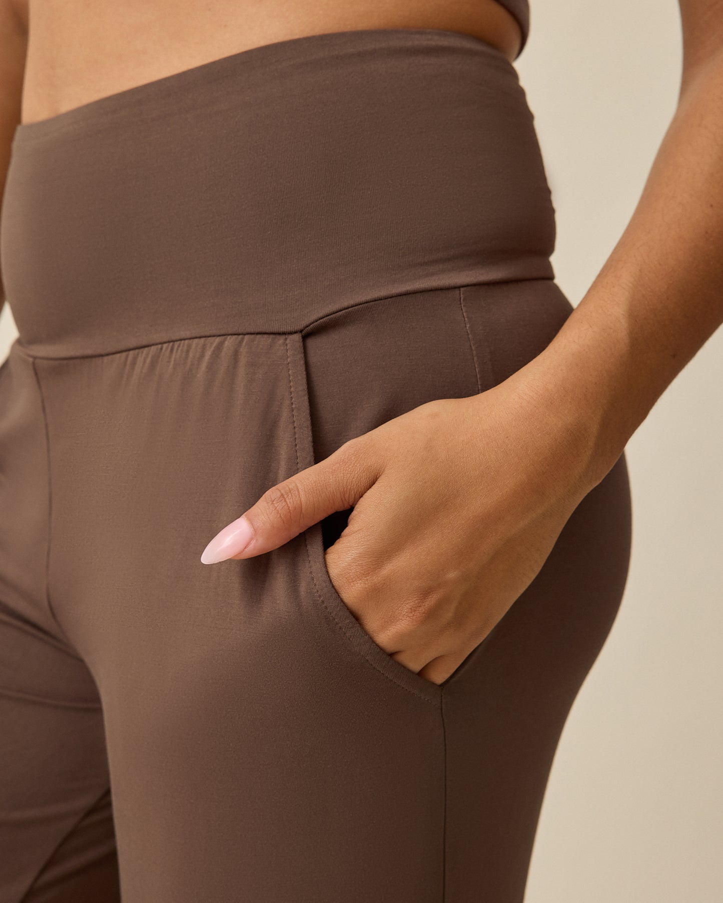 Model displaying pockets on Bamboo Wide Leg Maternity & Postpartum Lounge Pant in Chocolate on a beige background