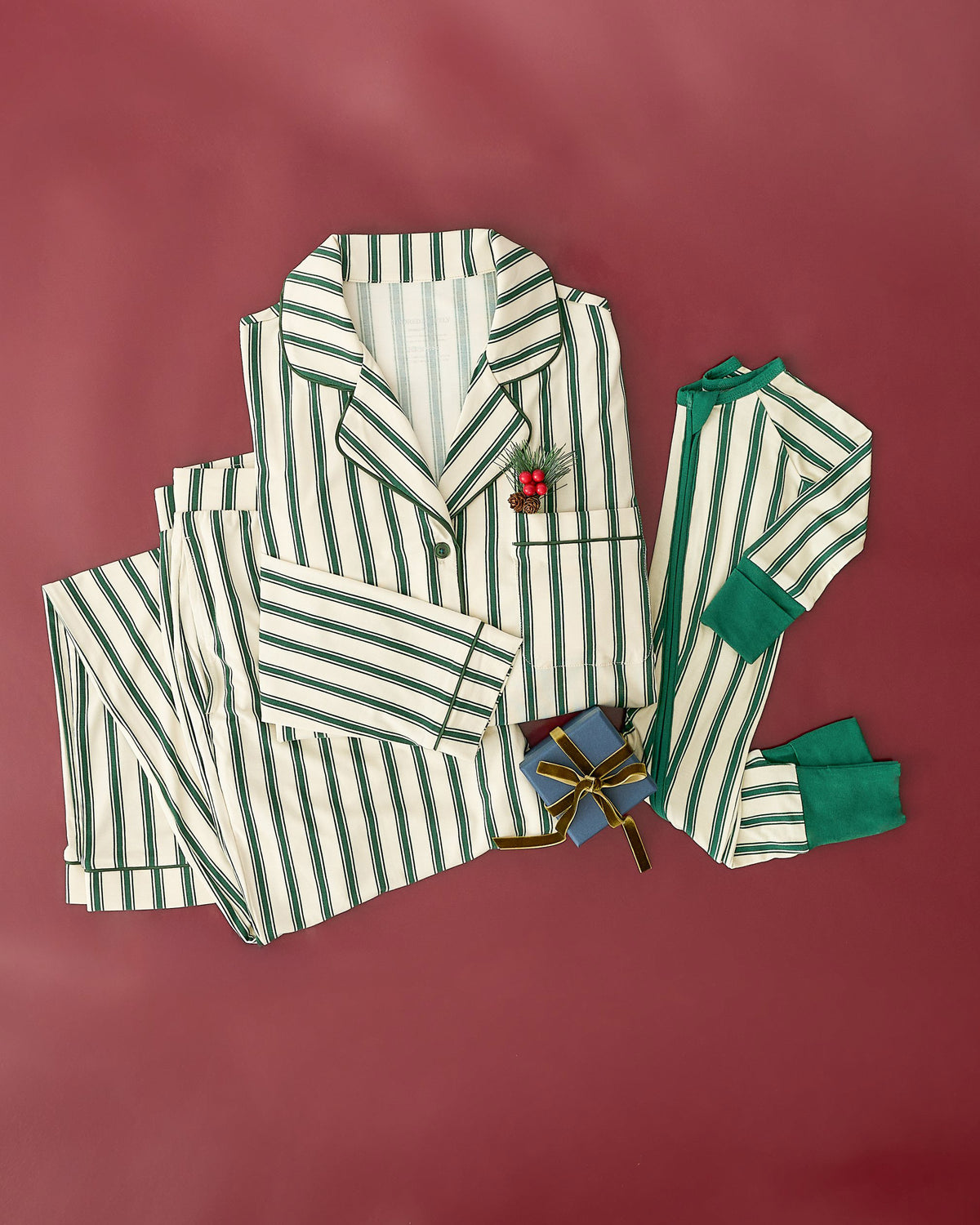 Bamboo Baby Pajama in Green Candy Stripe and Clea Bamboo Long Sleeve Pajama Set in Green Candy Stripe with a sprig of fir tree and little gift box, on a burgundy background.