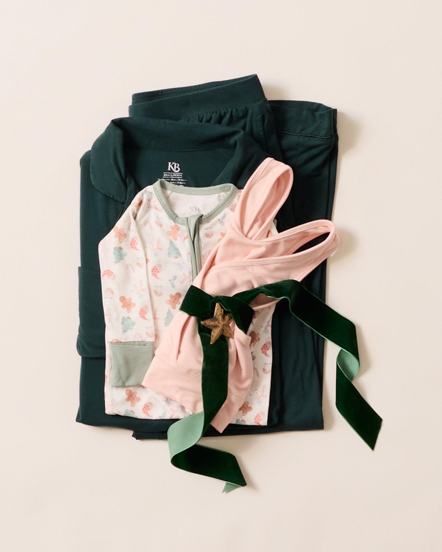 Folded dark green jacket with a pink baby outfit on a light beige background