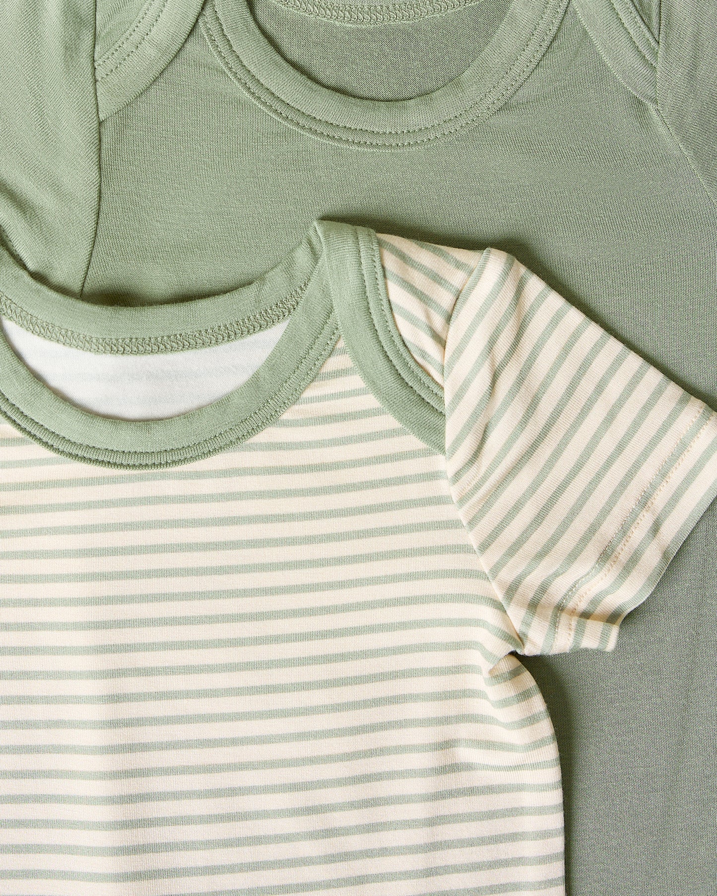 Close-up of two baby bodysuits, one sage candy stripe and one solid sage