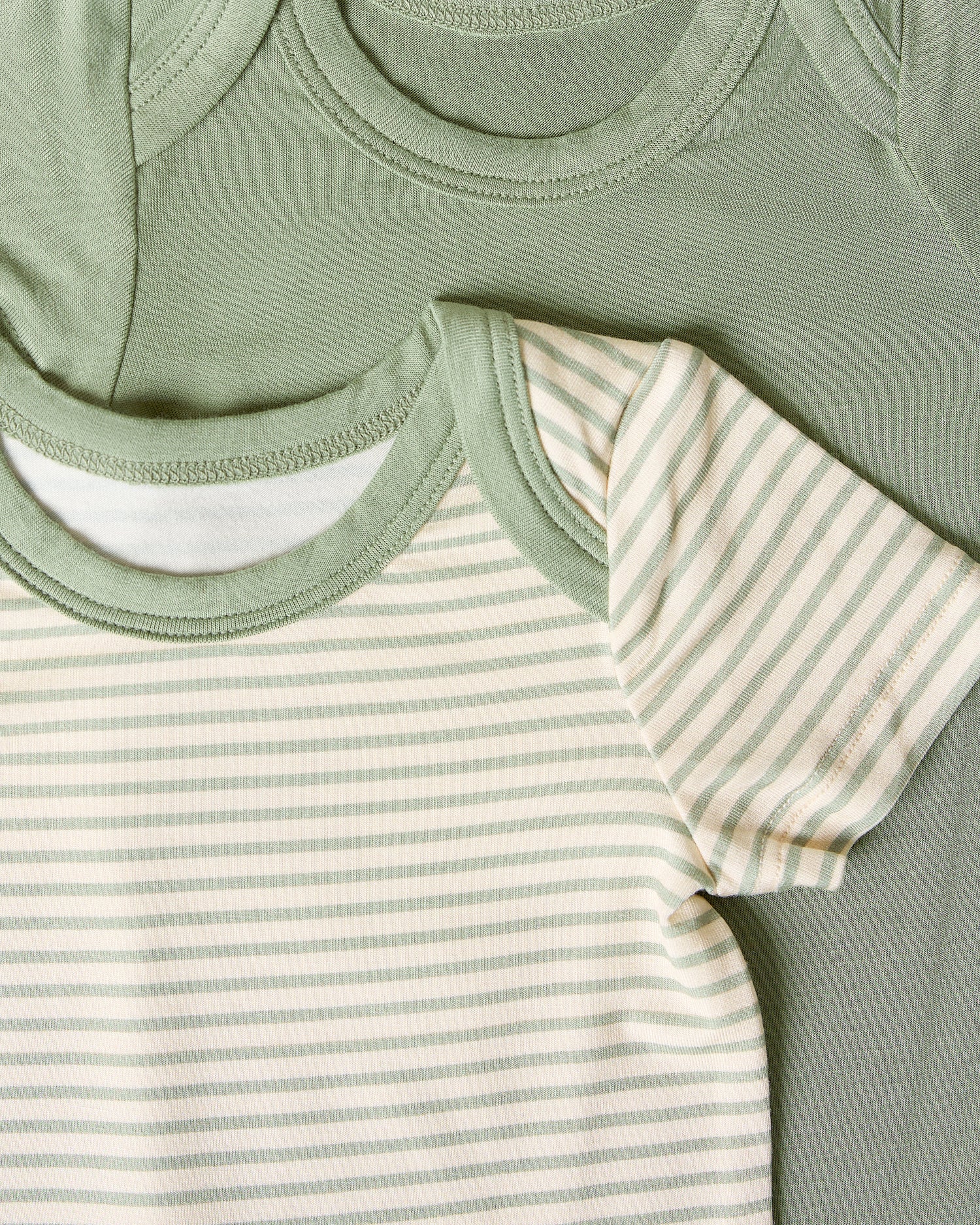 Close-up of two baby bodysuits, one sage candy stripe and one solid sage