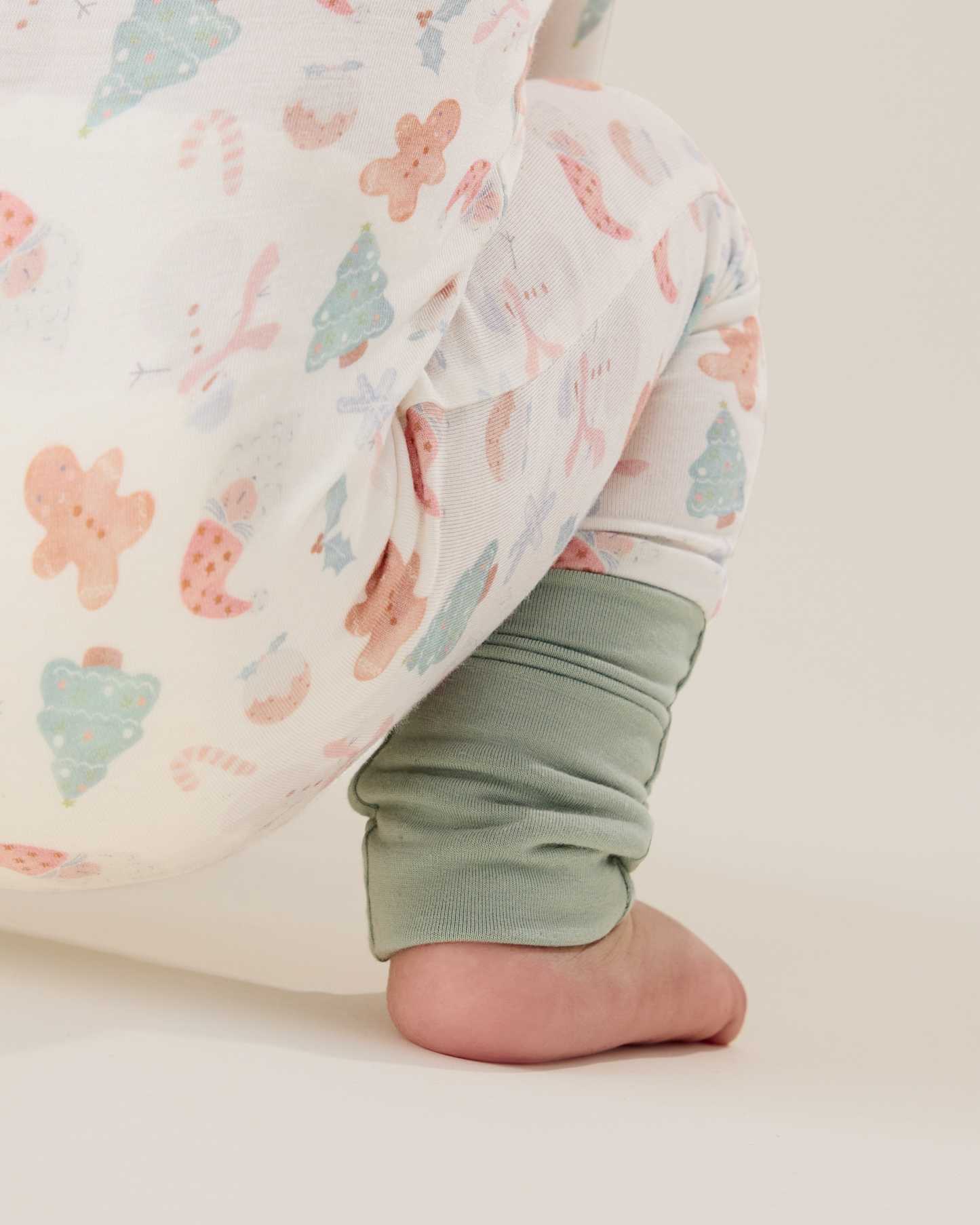 Baby wearing the Bamboo Baby Pajama in Cozy Holiday pattern - gingerbread men, Christmas trees, candy canes, Santa, snowmen, and showing light green ankle cuff