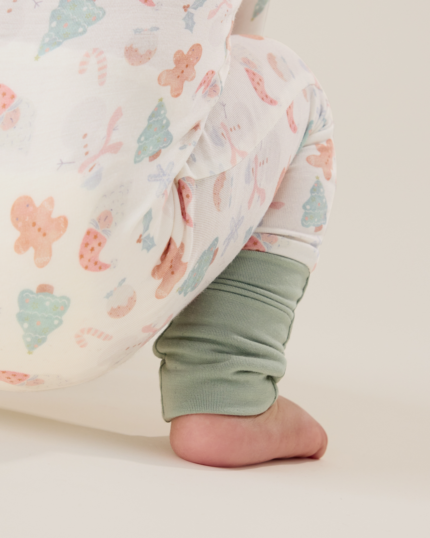 Baby wearing the Bamboo Baby Pajama in Cozy Holiday pattern - gingerbread men, Christmas trees, candy canes, Santa, snowmen, and showing light green ankle cuff