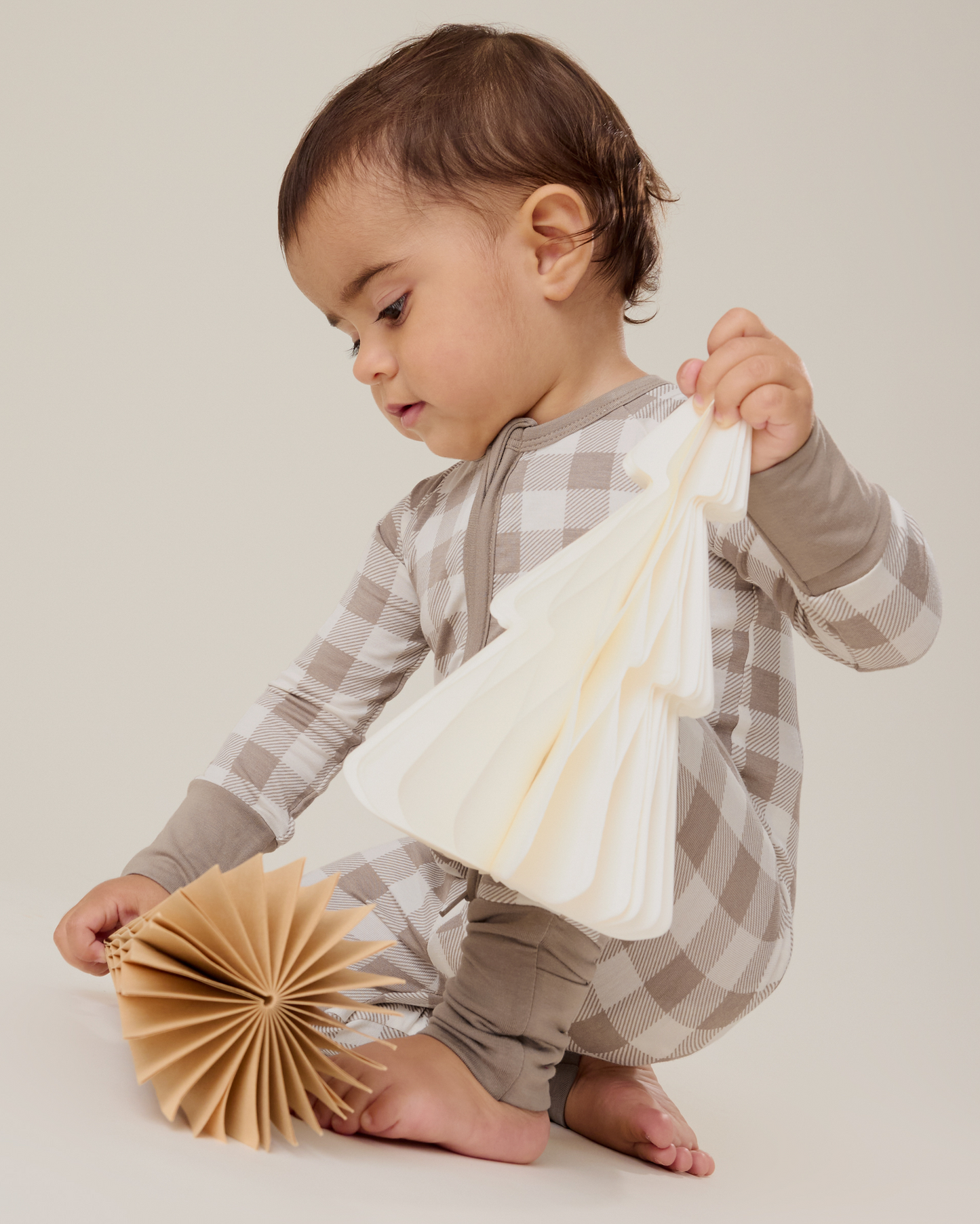 Baby sitting wearing the Bamboo Baby Pajama in Taupe Gingham playing with paper trees