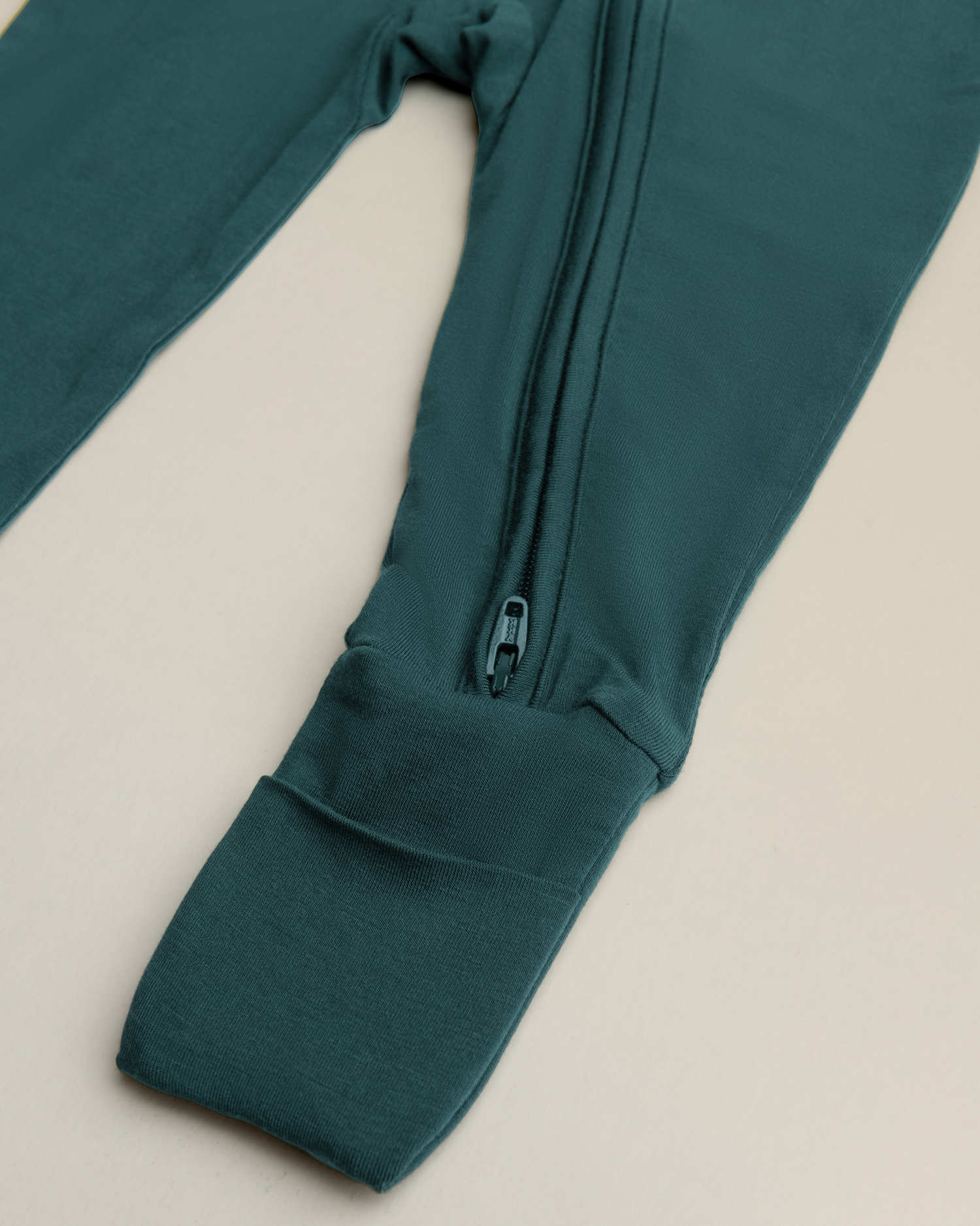 Bamboo Baby Pajamas in Evergreen with a zipper detial on a beige background