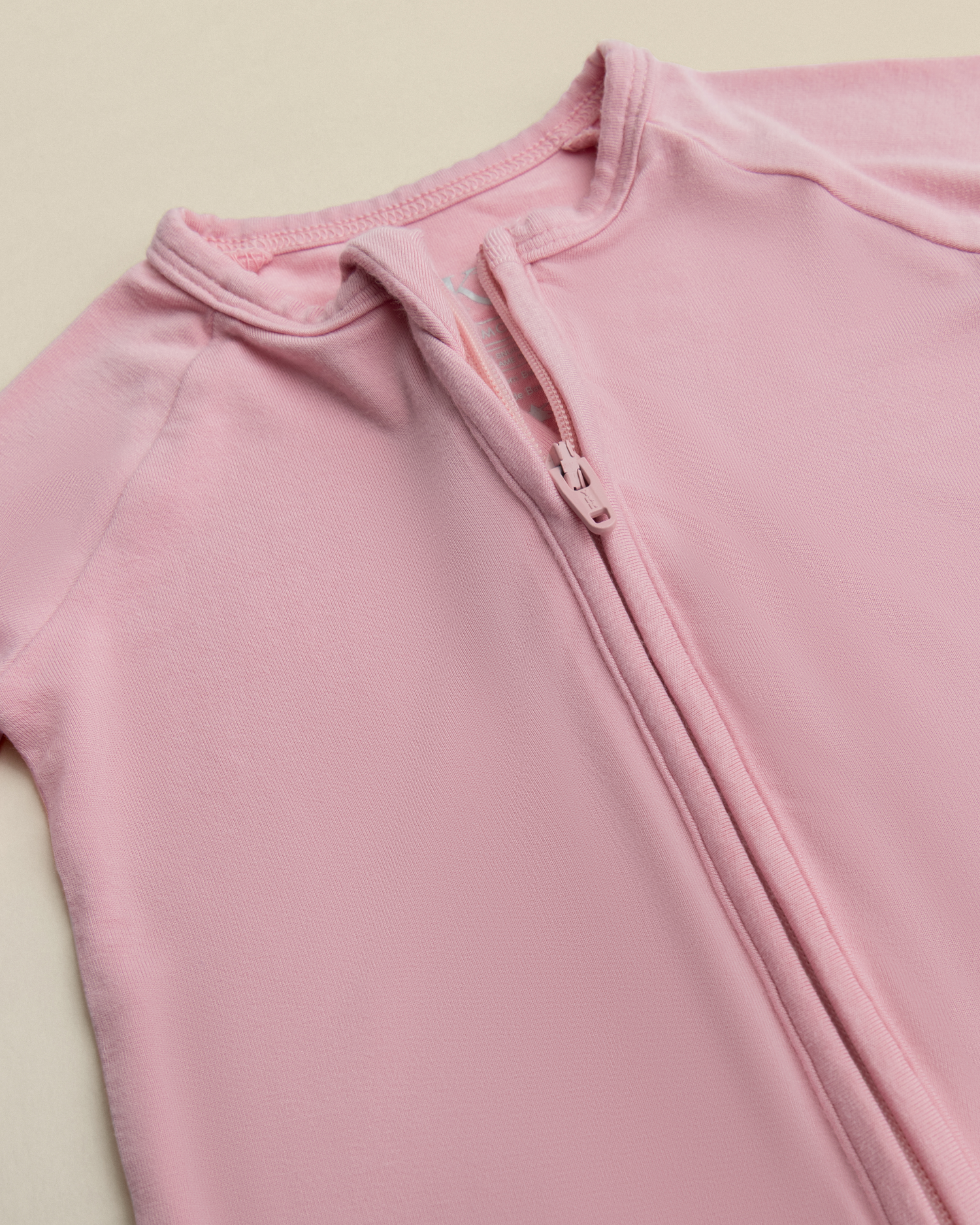 Close-up of Bamboo Baby Pajamas in Light Mauve with a zipper on a beige background