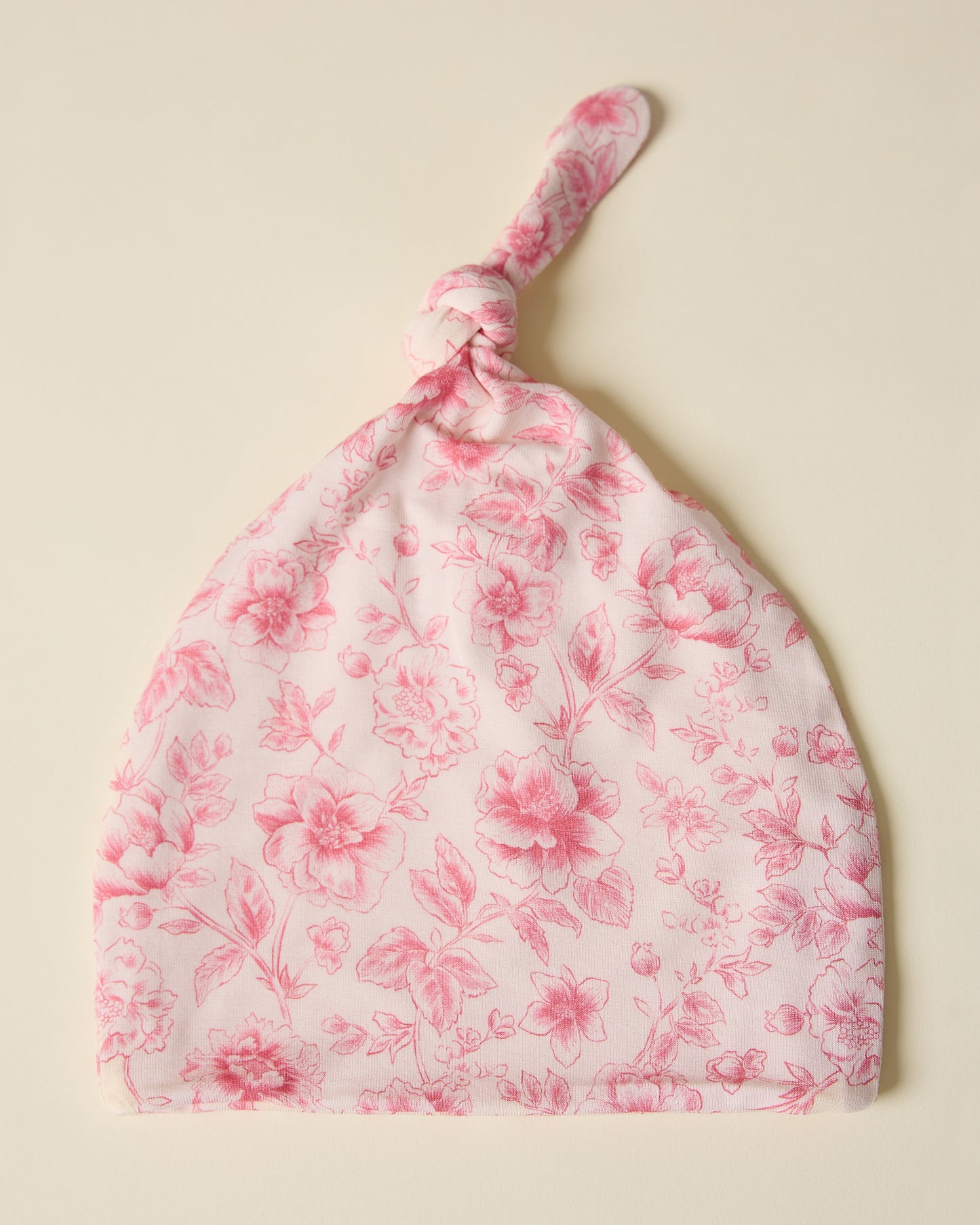 Floral patterned baby hat in pink toile on a beige background