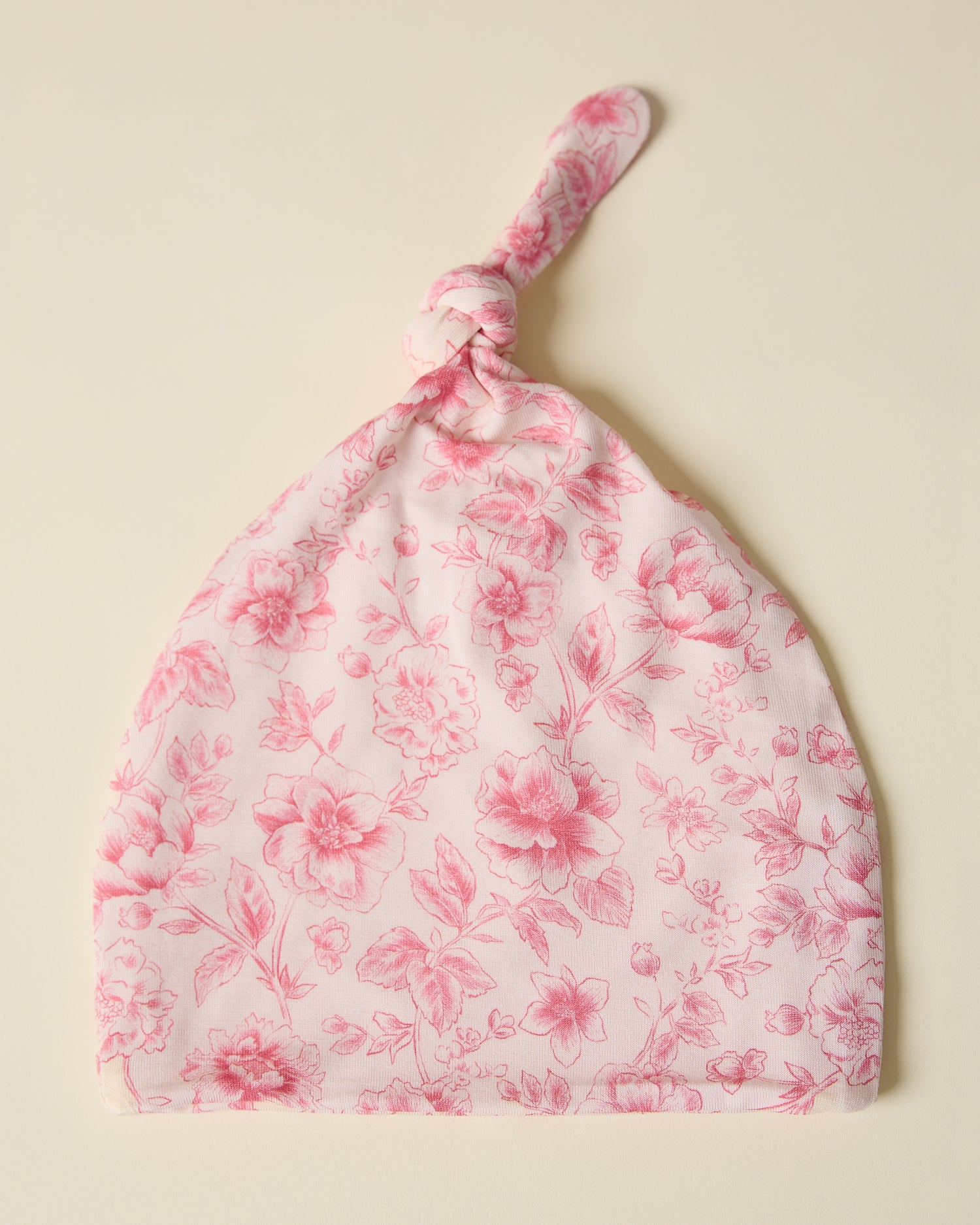 Floral patterned baby hat in pink toile on a beige background
