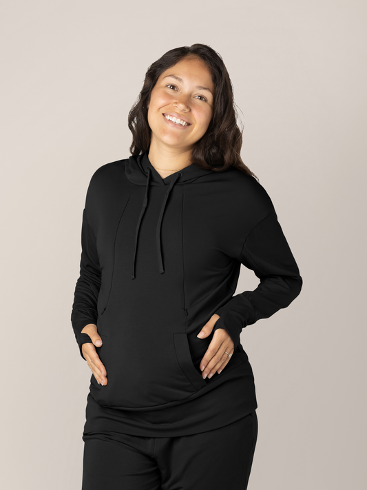 Model wearing the Bamboo Nursing Hoodie in Black with her hands on her pregnant belly. @model_info:Desiree is wearing a Small.